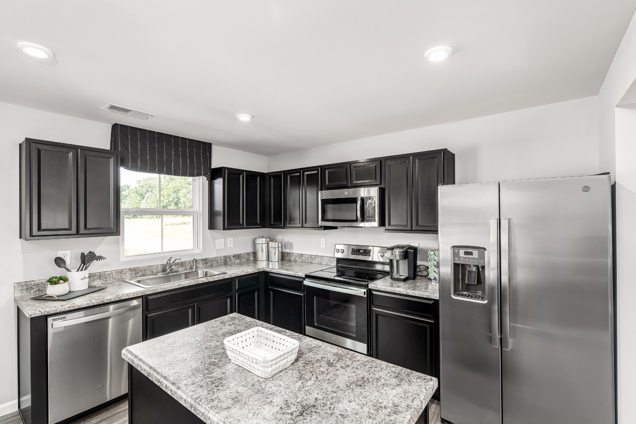 Kitchen with black cabinets, granite counters, a central island, and stainless steel appliances.