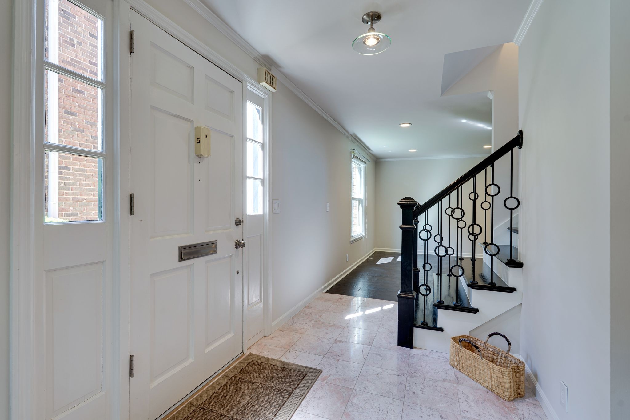 Entry foyer with a white paneled door, pale tile floor, and black iron staircase railing.