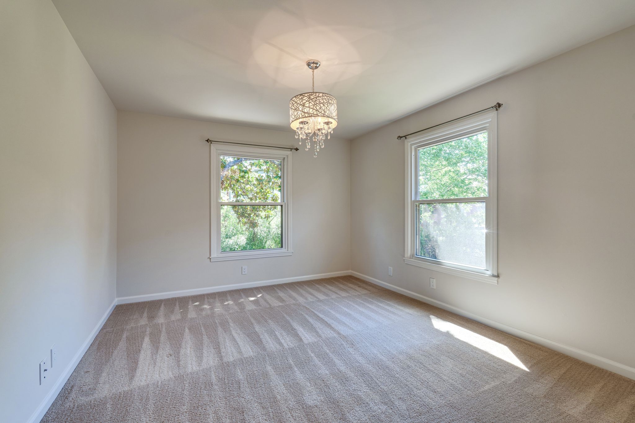 Empty carpeted bedroom with two large windows and a crystal chandelier.