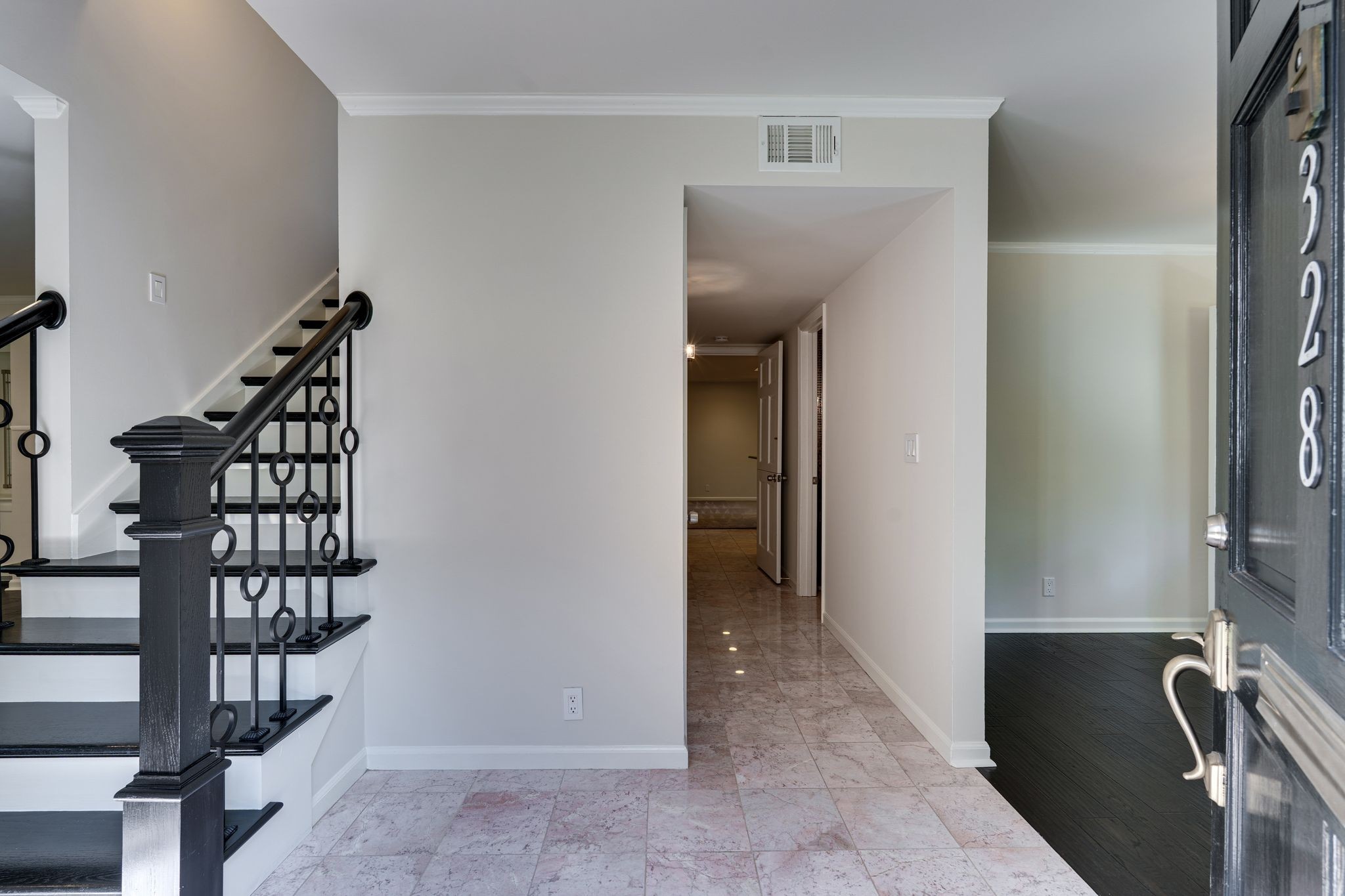 Entry foyer with a black-railed staircase, stone tile floor, and open front door.