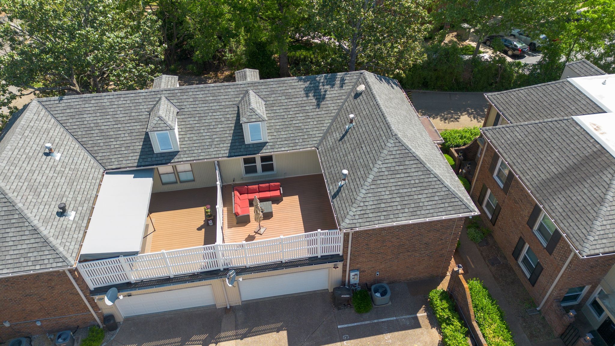 Aerial view of a brick townhome with a furnished deck and red sectional seating.