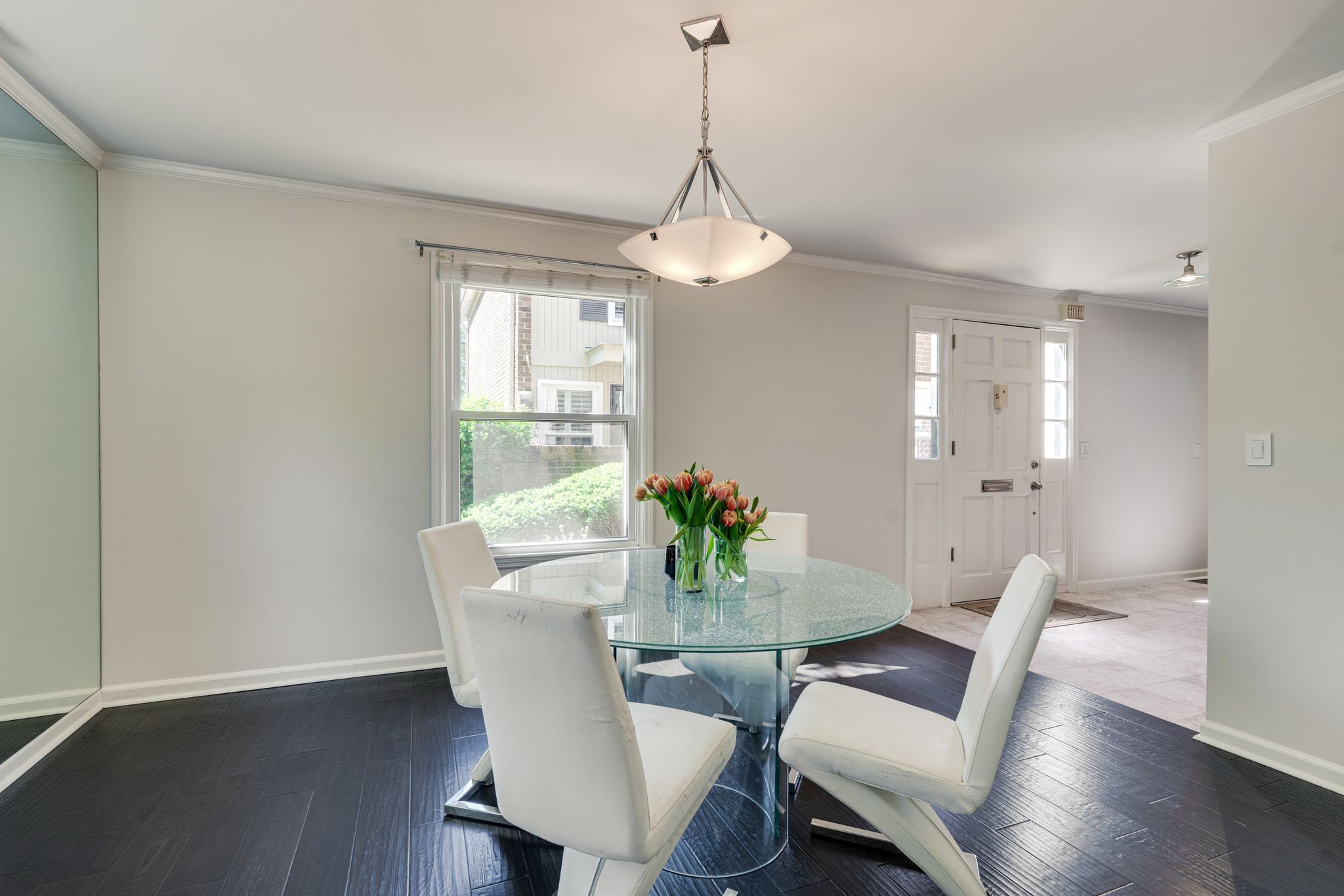 Dining room with a glass table, white chairs, tulips, and dark wood flooring.
