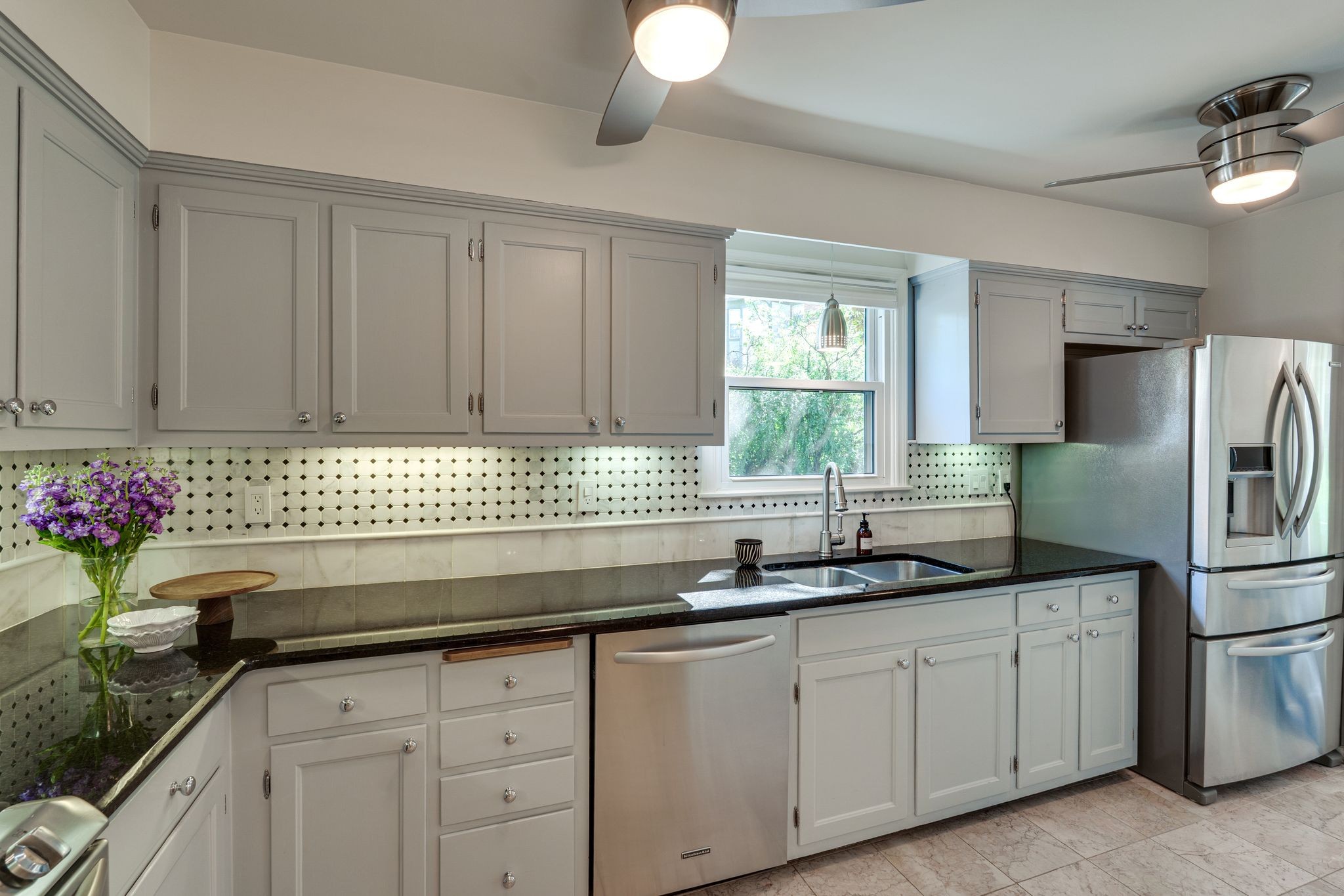 Kitchen with gray cabinets, black countertops, patterned tile backsplash, and stainless steel appliances.