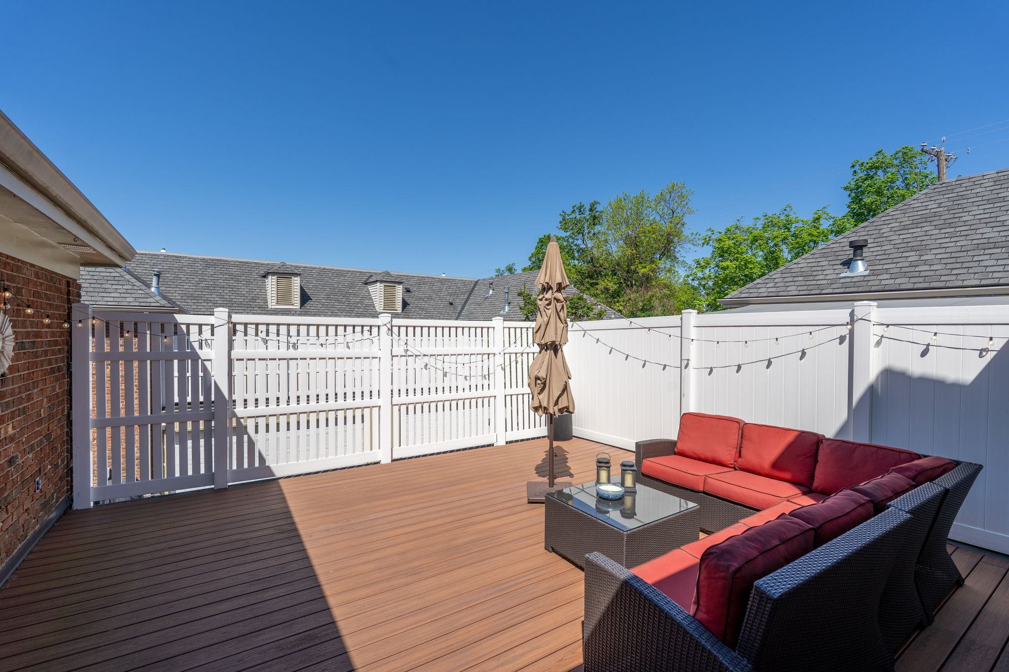 Rooftop deck with white fencing, string lights, and red-cushioned wicker seating.