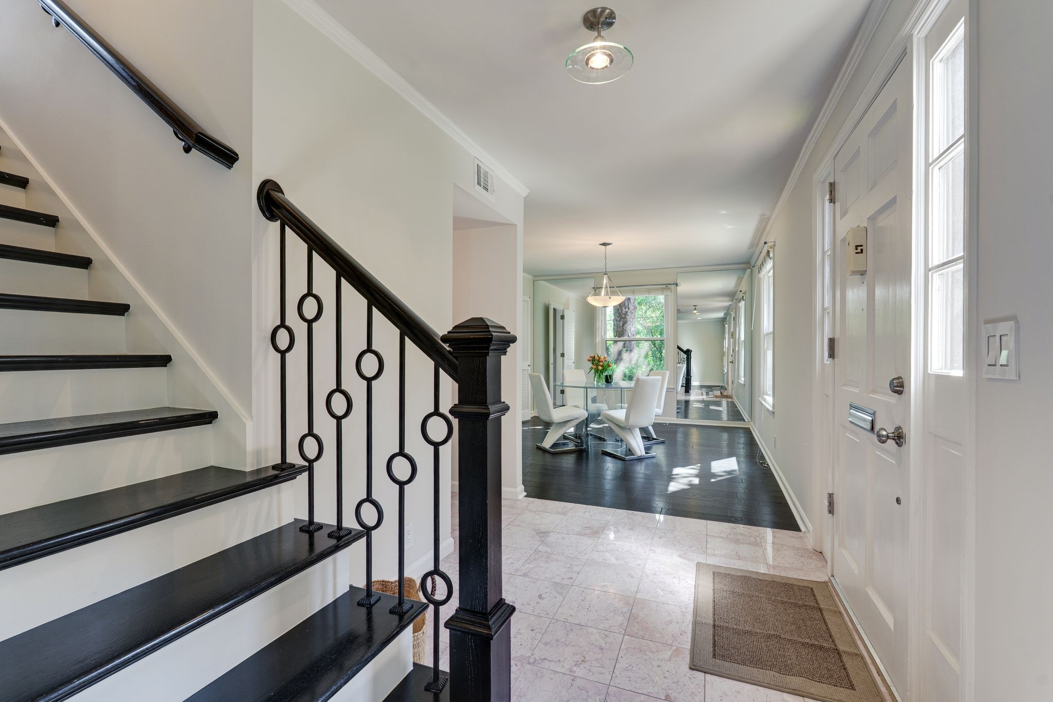 Entry foyer with a black-railed staircase leading toward a sunlit dining area.
