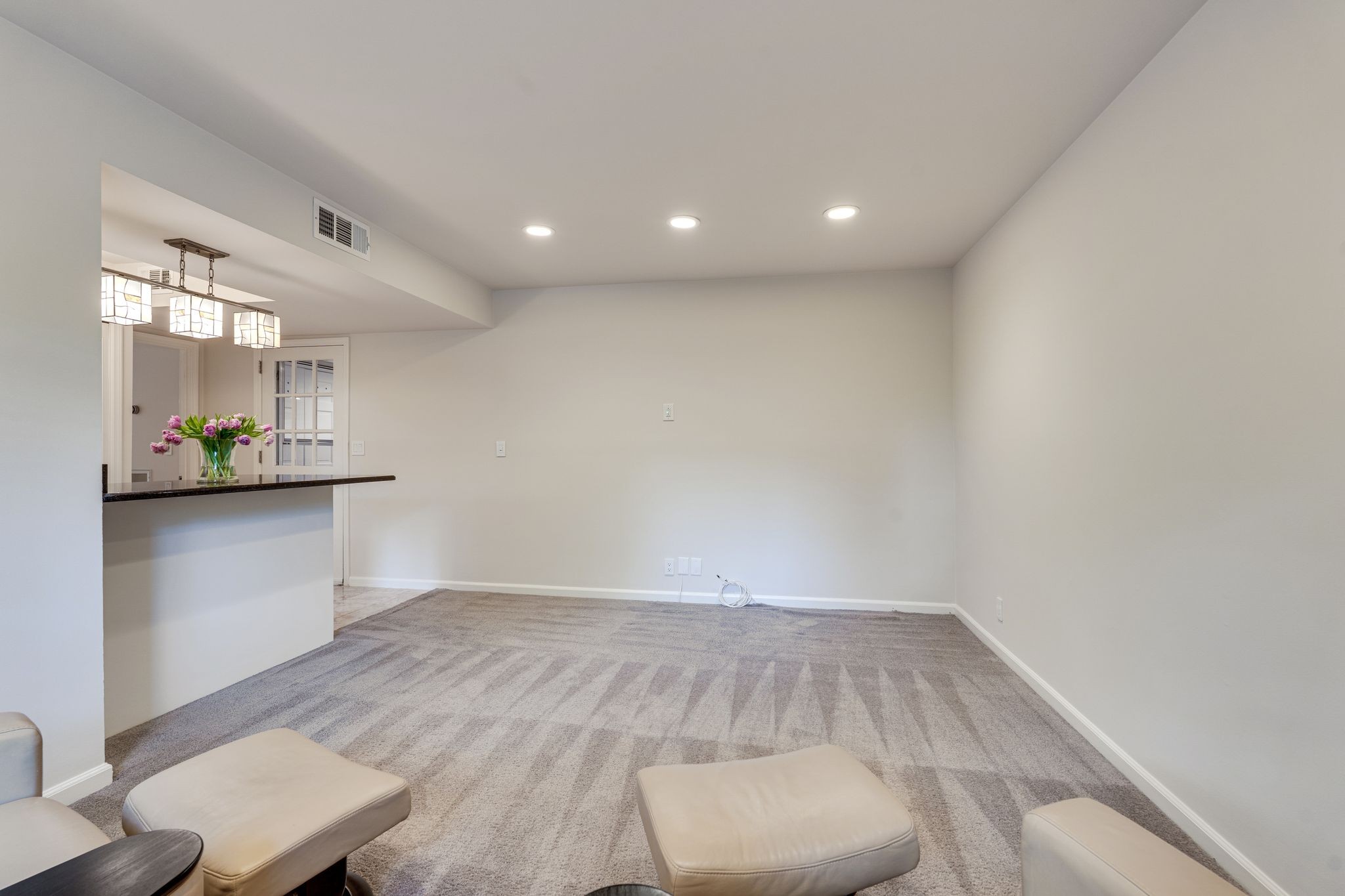 Carpeted living room with recessed lights, a pass-through counter, and a few upholstered ottomans.