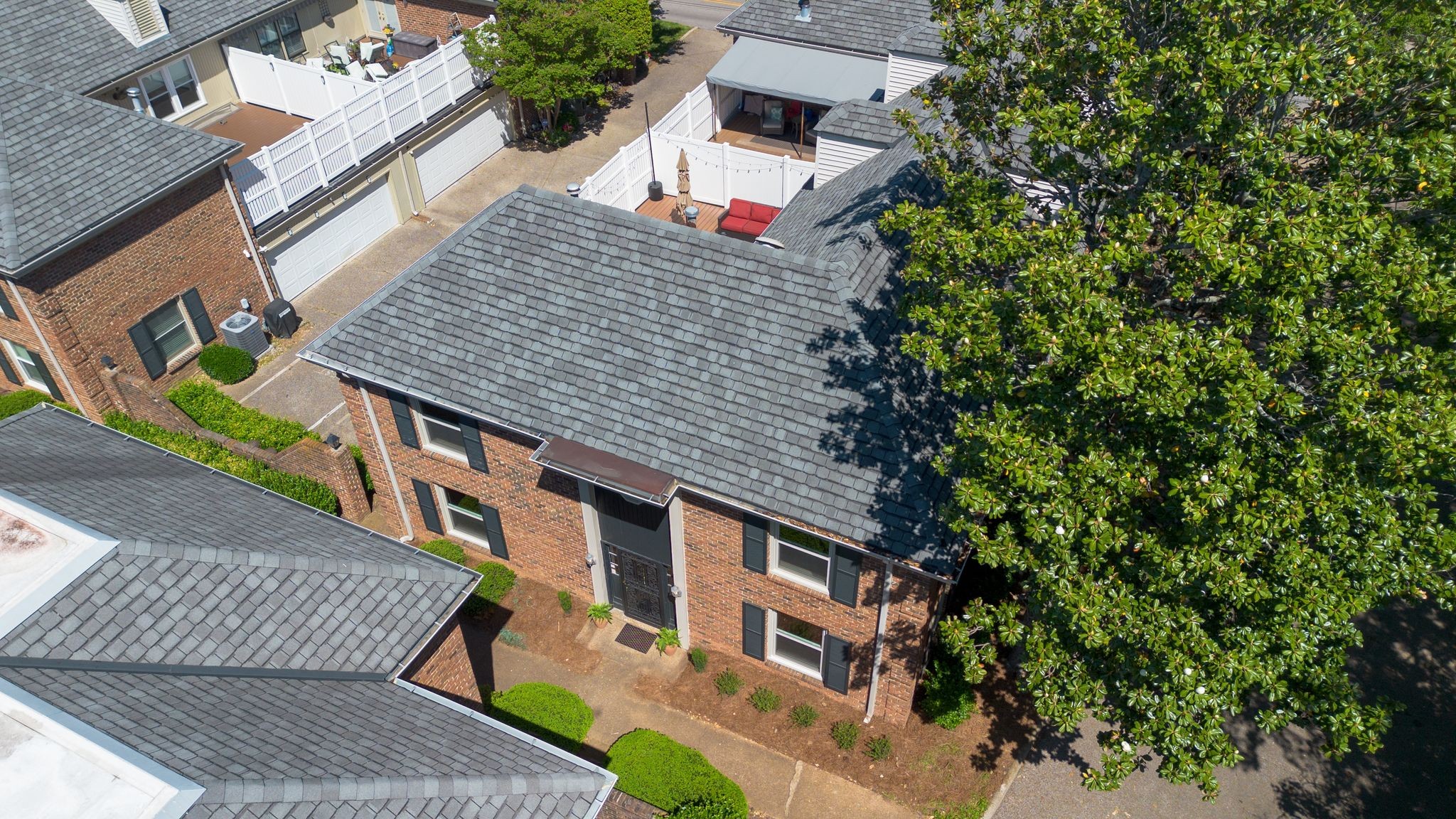 Aerial view of brick homes with fenced decks, gray roofs, and mature trees.