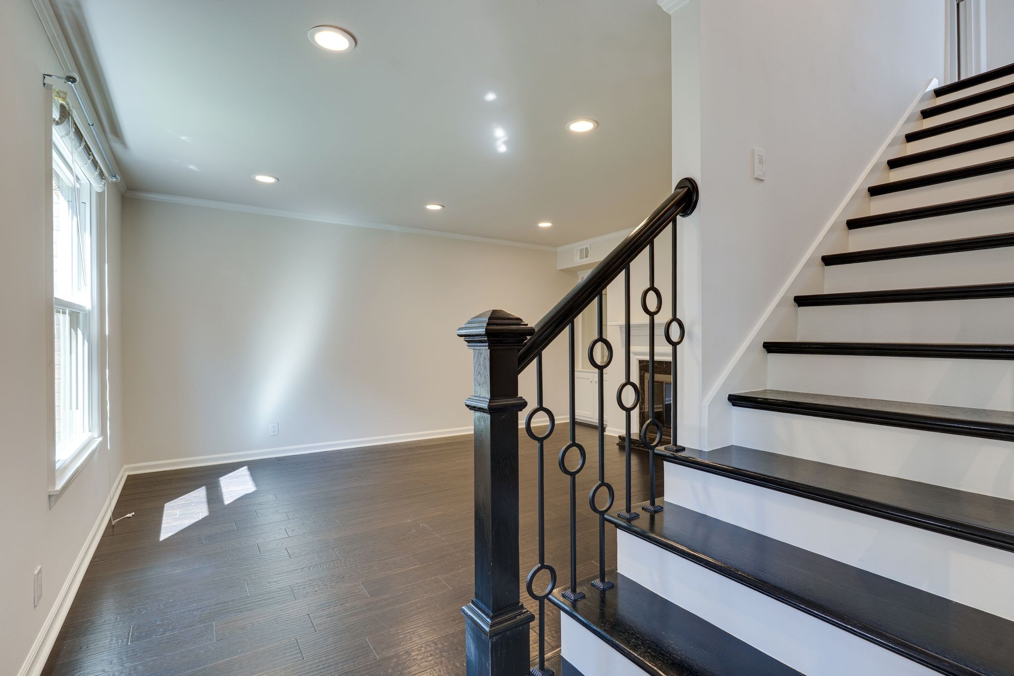 Vacant room beside a dark wood staircase with decorative black metal railing and tall windows.