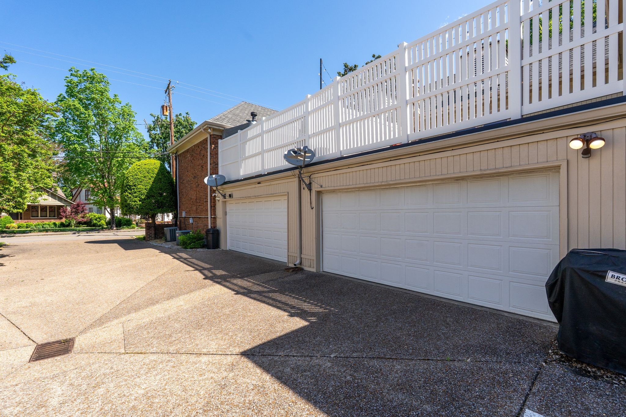 Attached garages beneath a long white-railed deck, viewed from the paved driveway.