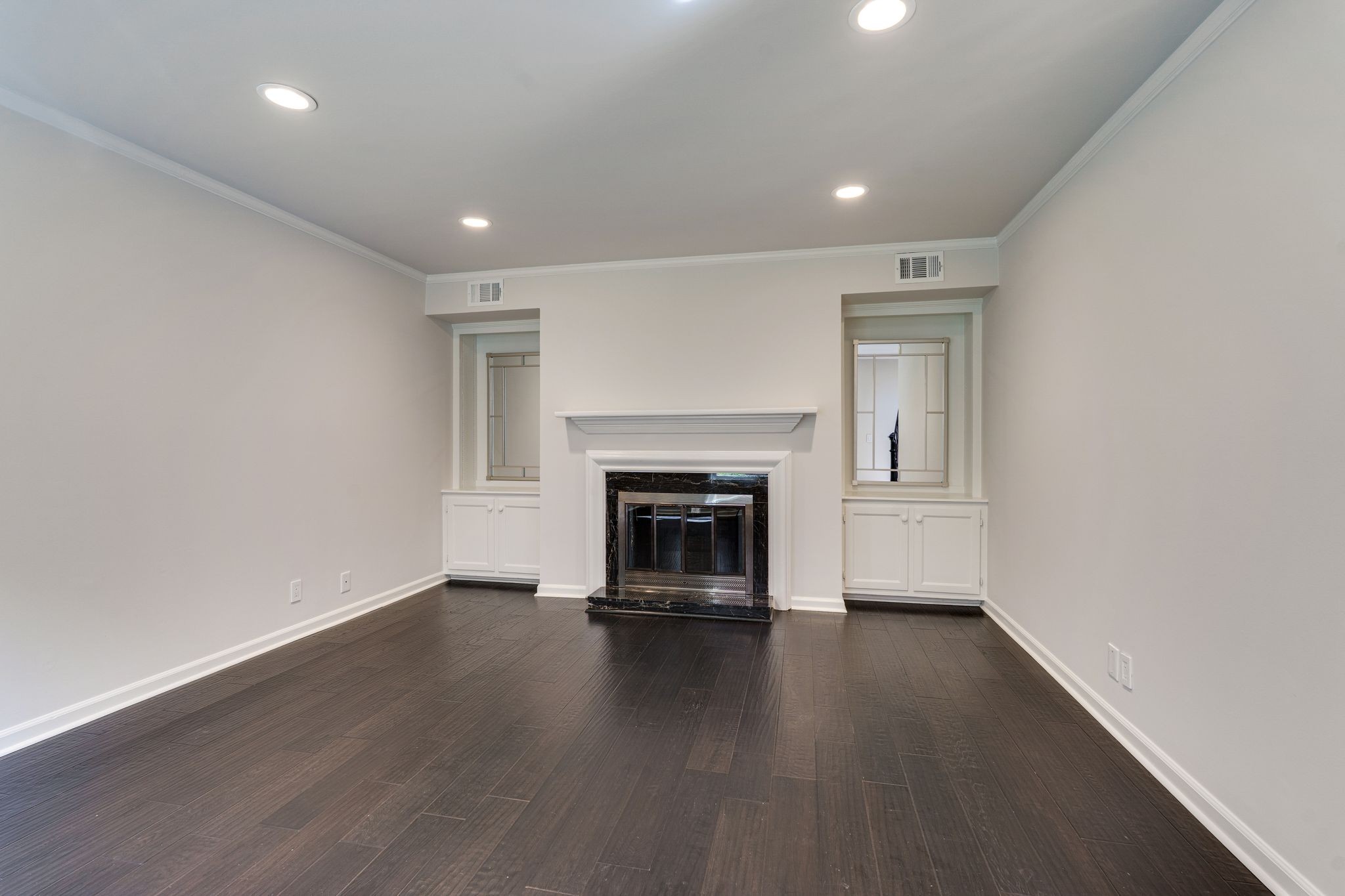 Empty room with dark wood floors, a fireplace, and built-in cabinets.