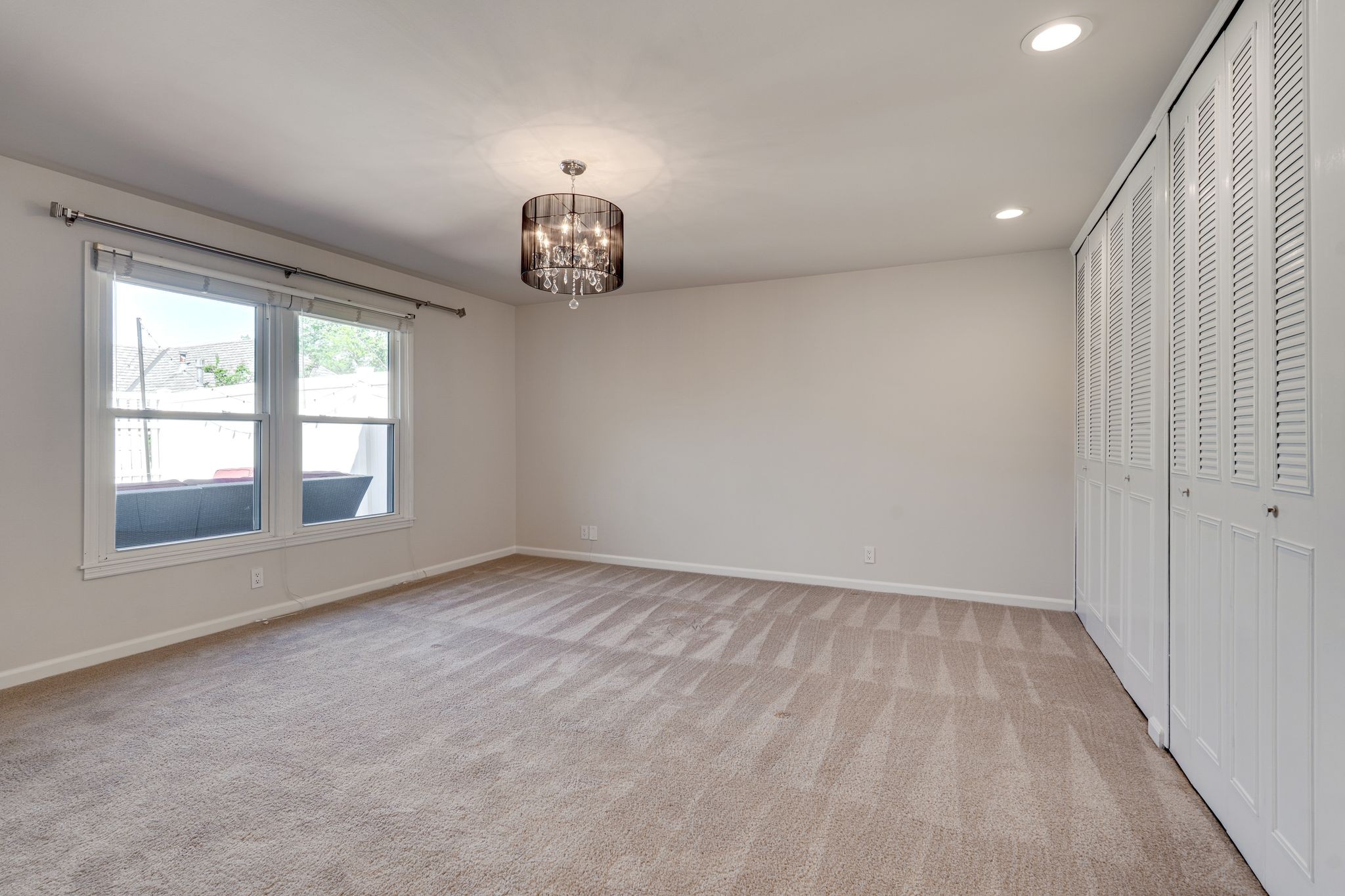 Empty bedroom with louvered closets, two windows, and a chandelier.