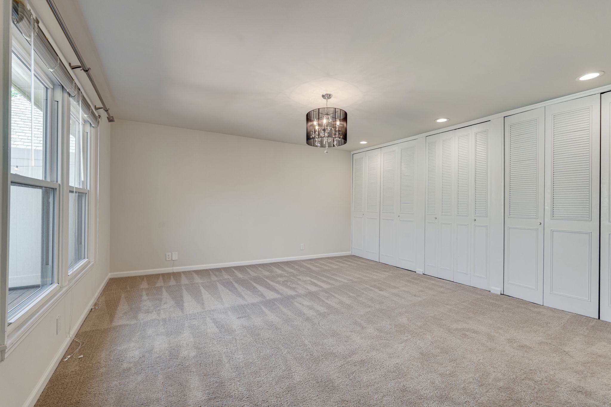 Empty bedroom with tall windows, wall of white closet doors, and a dark glass pendant light.