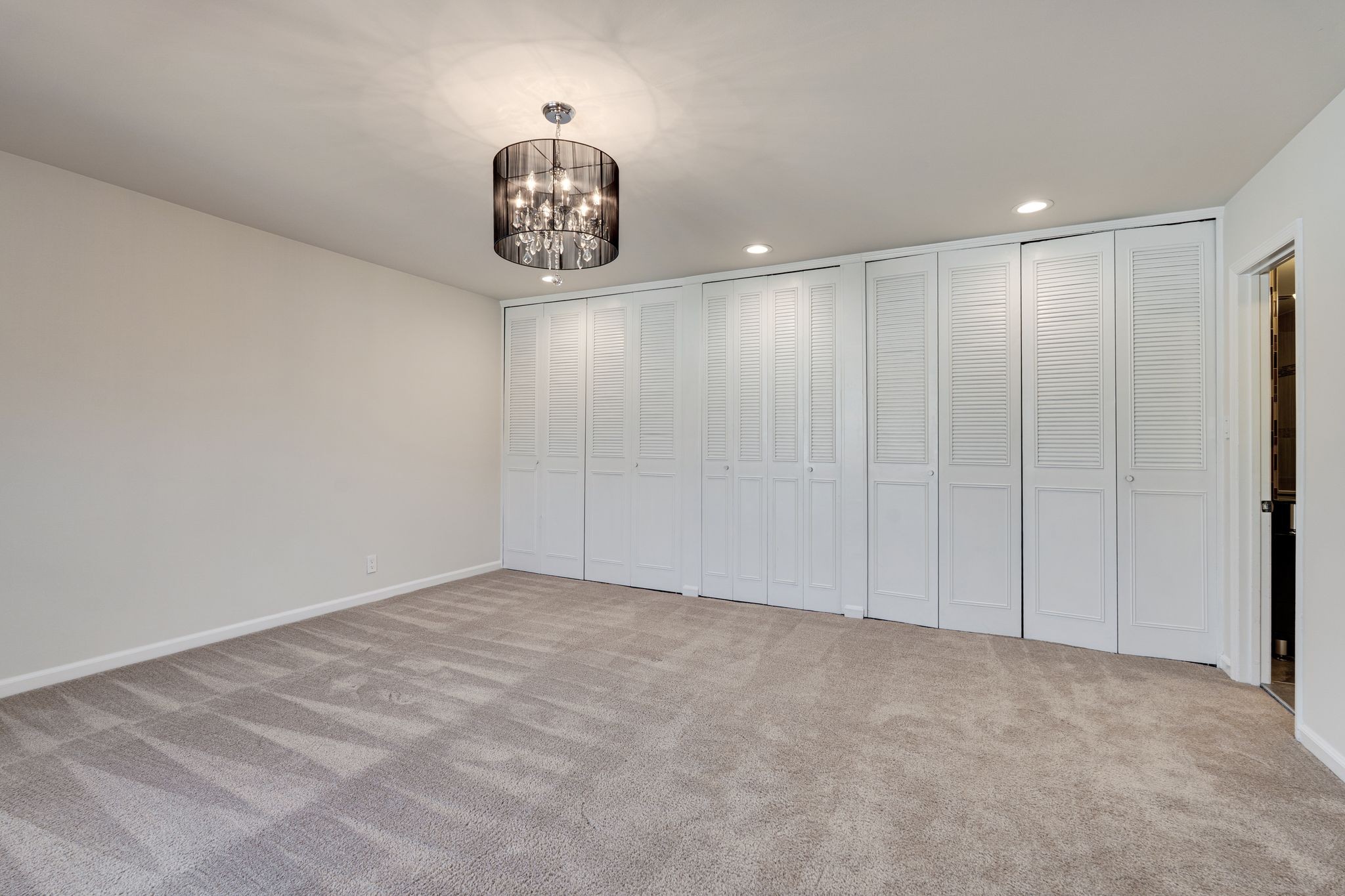 Empty carpeted room with white louvered closet doors and a dark chandelier.