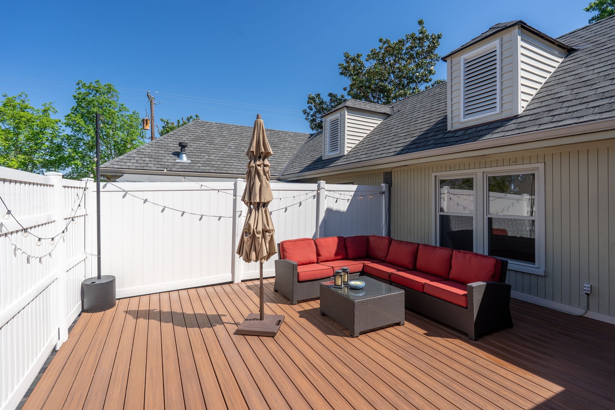 Furnished rooftop deck with red sectional seating, a closed umbrella, and white privacy fencing.