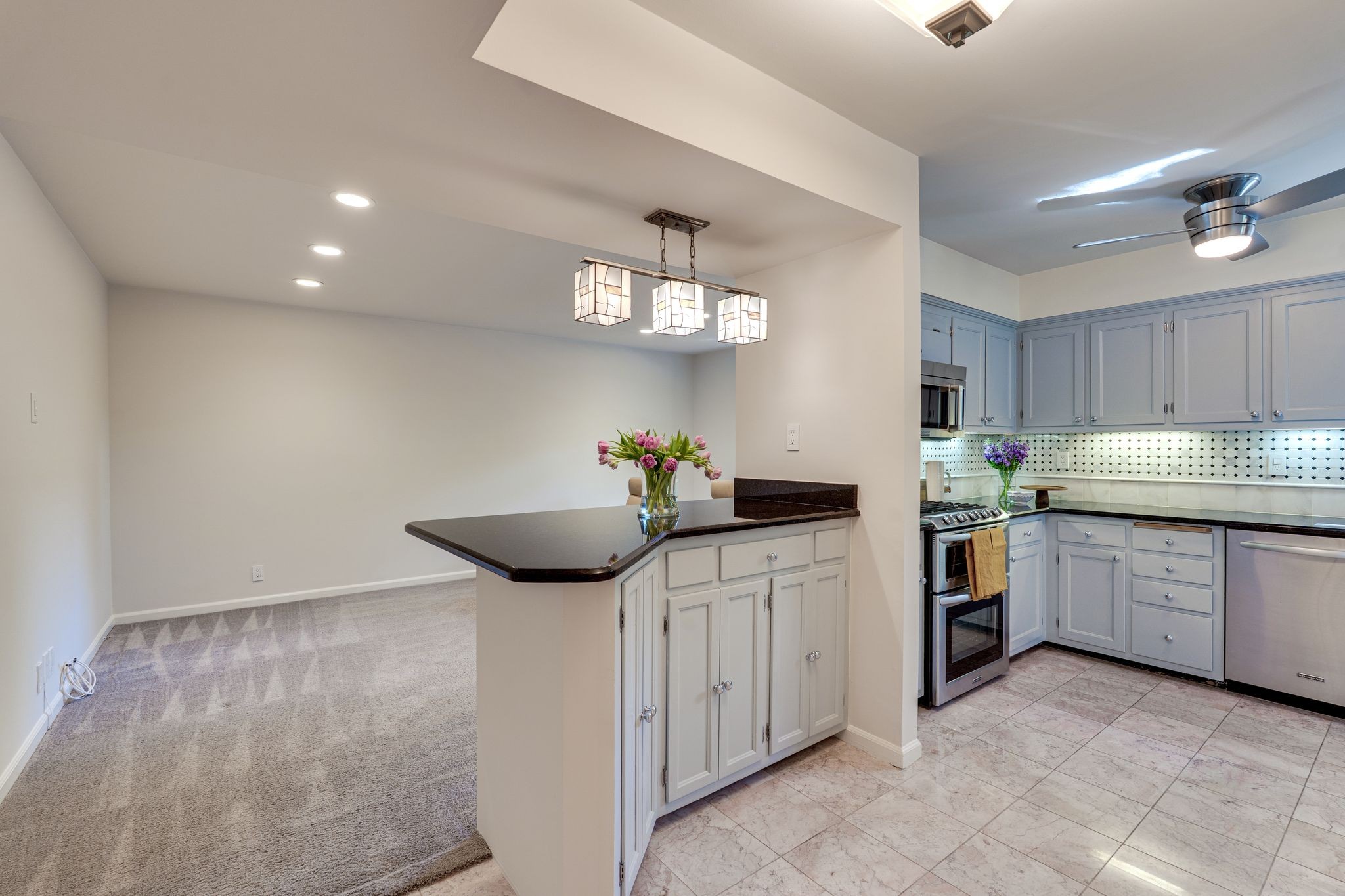 Kitchen with pale blue-gray cabinets, stainless appliances, and a dark stone breakfast bar beside a carpeted room.