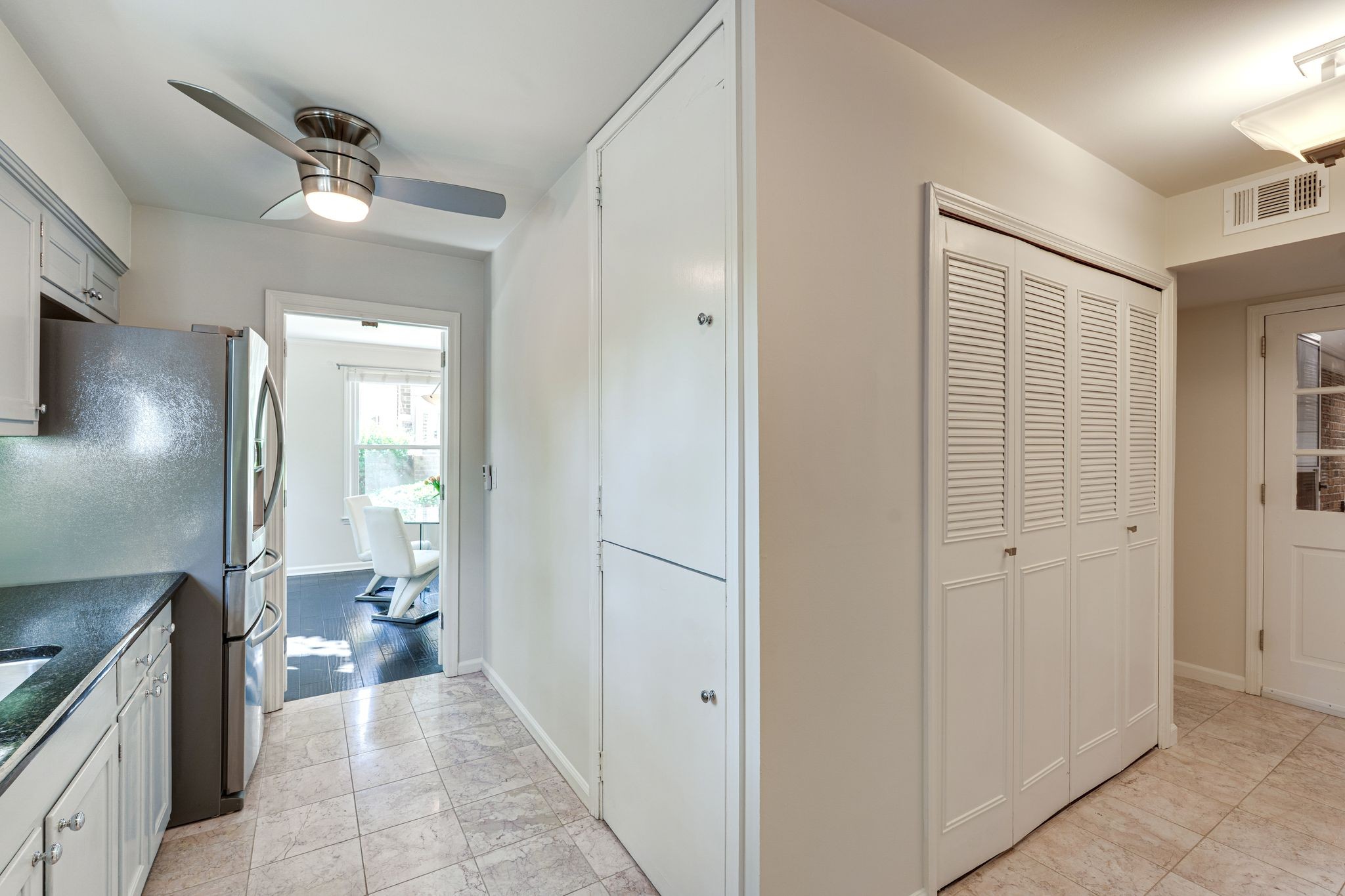 Kitchen with white cabinetry, stainless steel refrigerator, dark counters, and louvered closet doors.