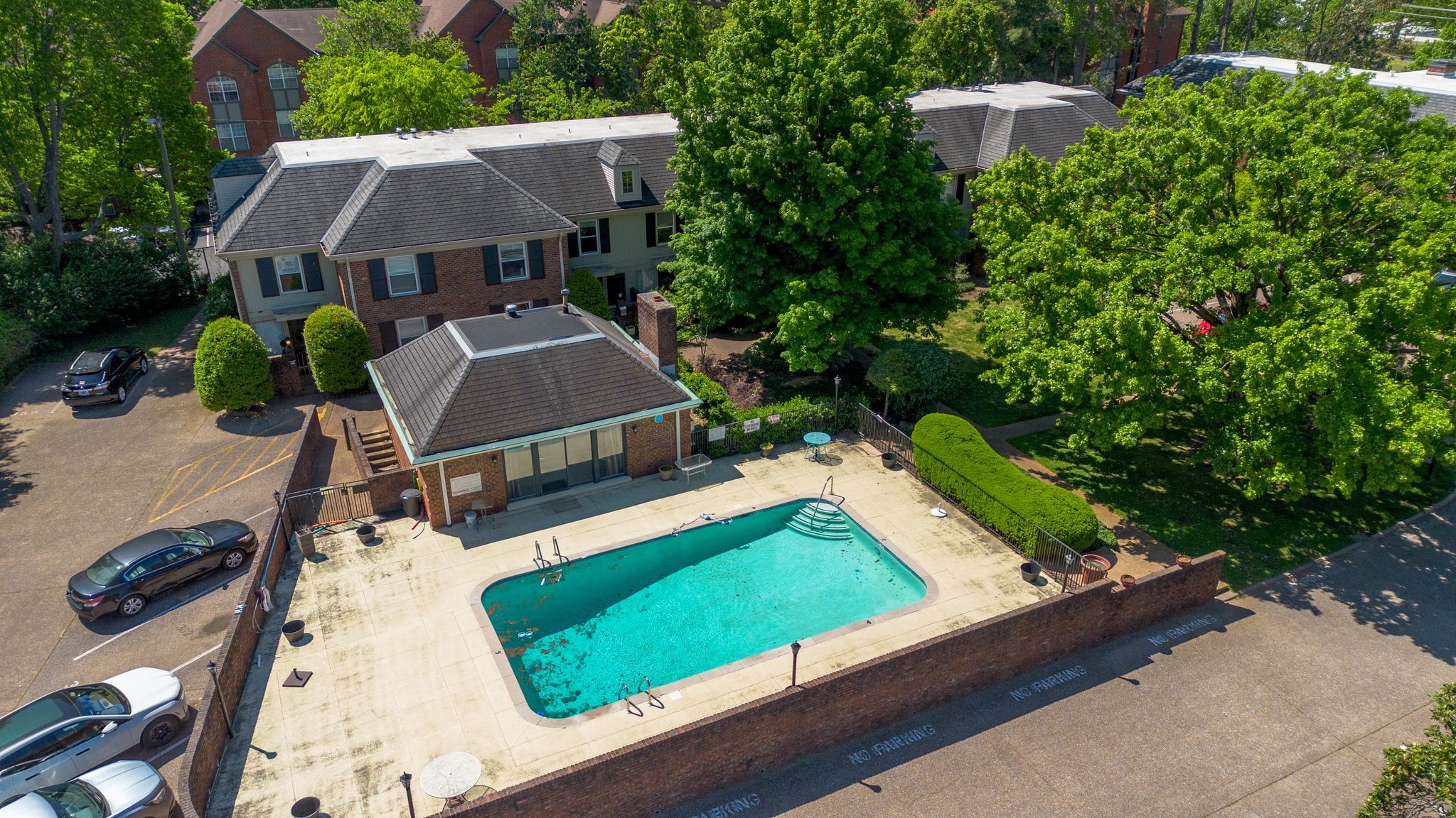 Aerial view of a brick residential property with a turquoise swimming pool and surrounding landscaped grounds.