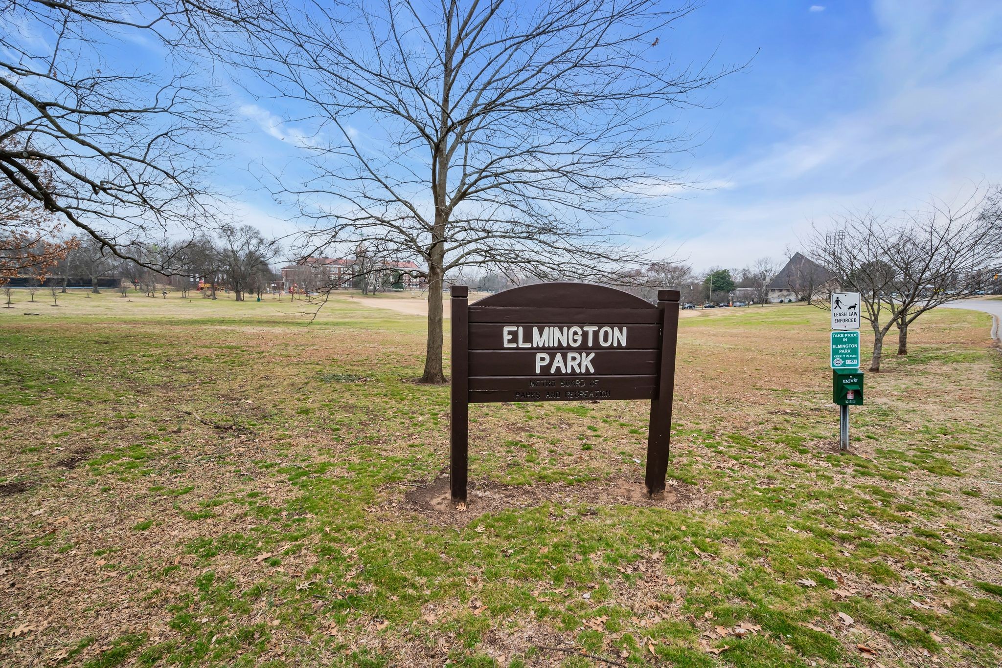 Elmington Park sign in a grassy park with leafless trees and a nearby leash-law sign.