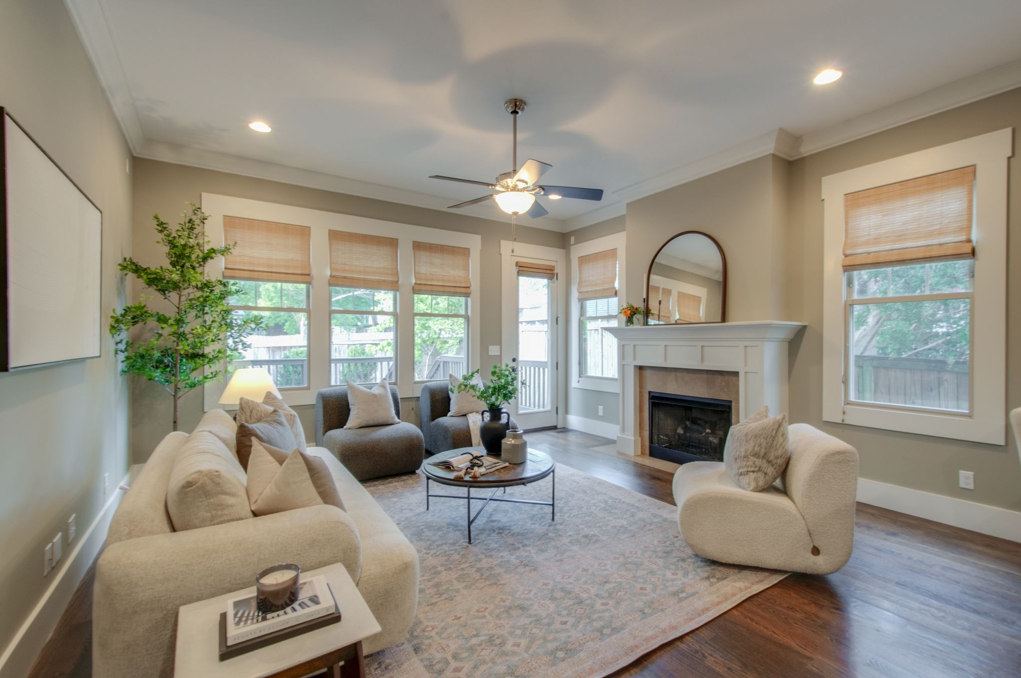 Staged living room with a white fireplace, cream seating, and large shaded windows.