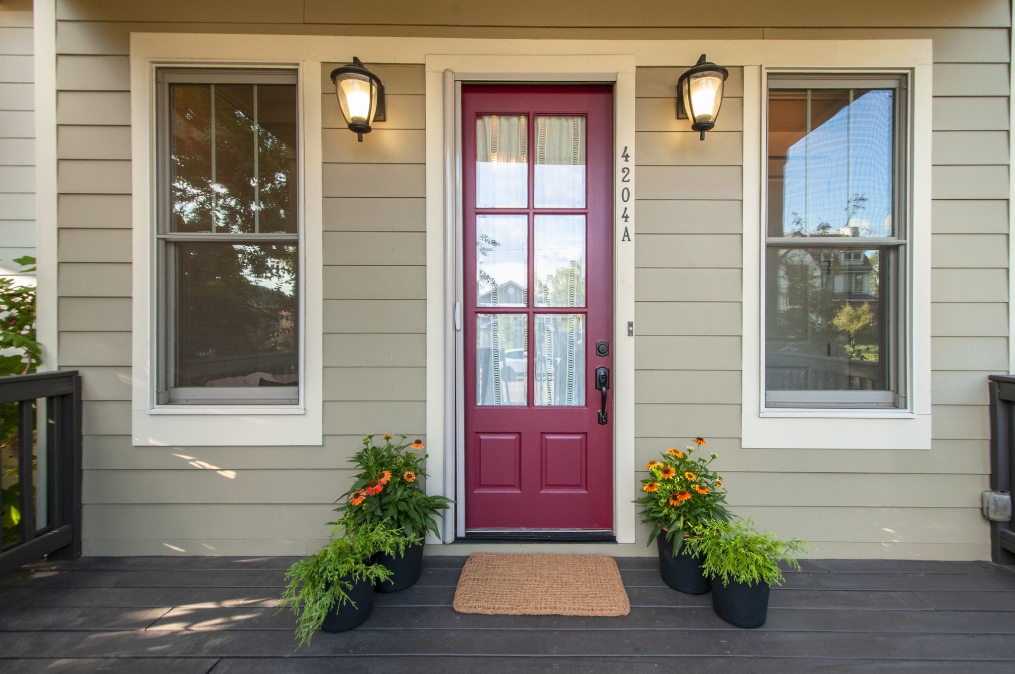 Home entrance with a burgundy glass-paneled door, flanked by windows and flowering porch planters.