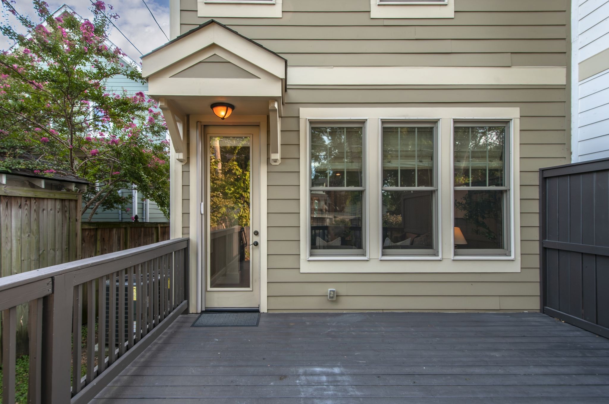 Townhouse exterior with a covered glass-door entry, three windows, and a deck beside a flowering tree.