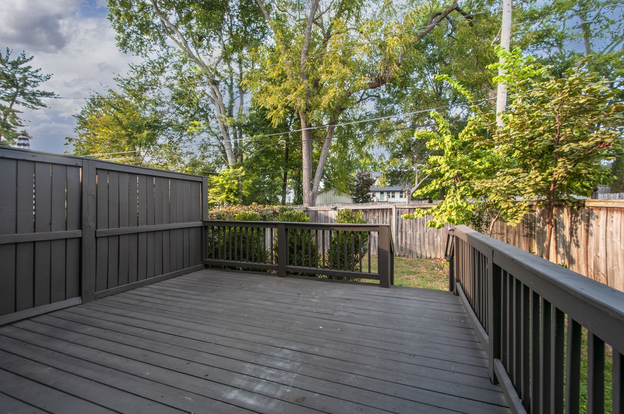 Wooden deck with dark railings overlooking a fenced, tree-shaded backyard.