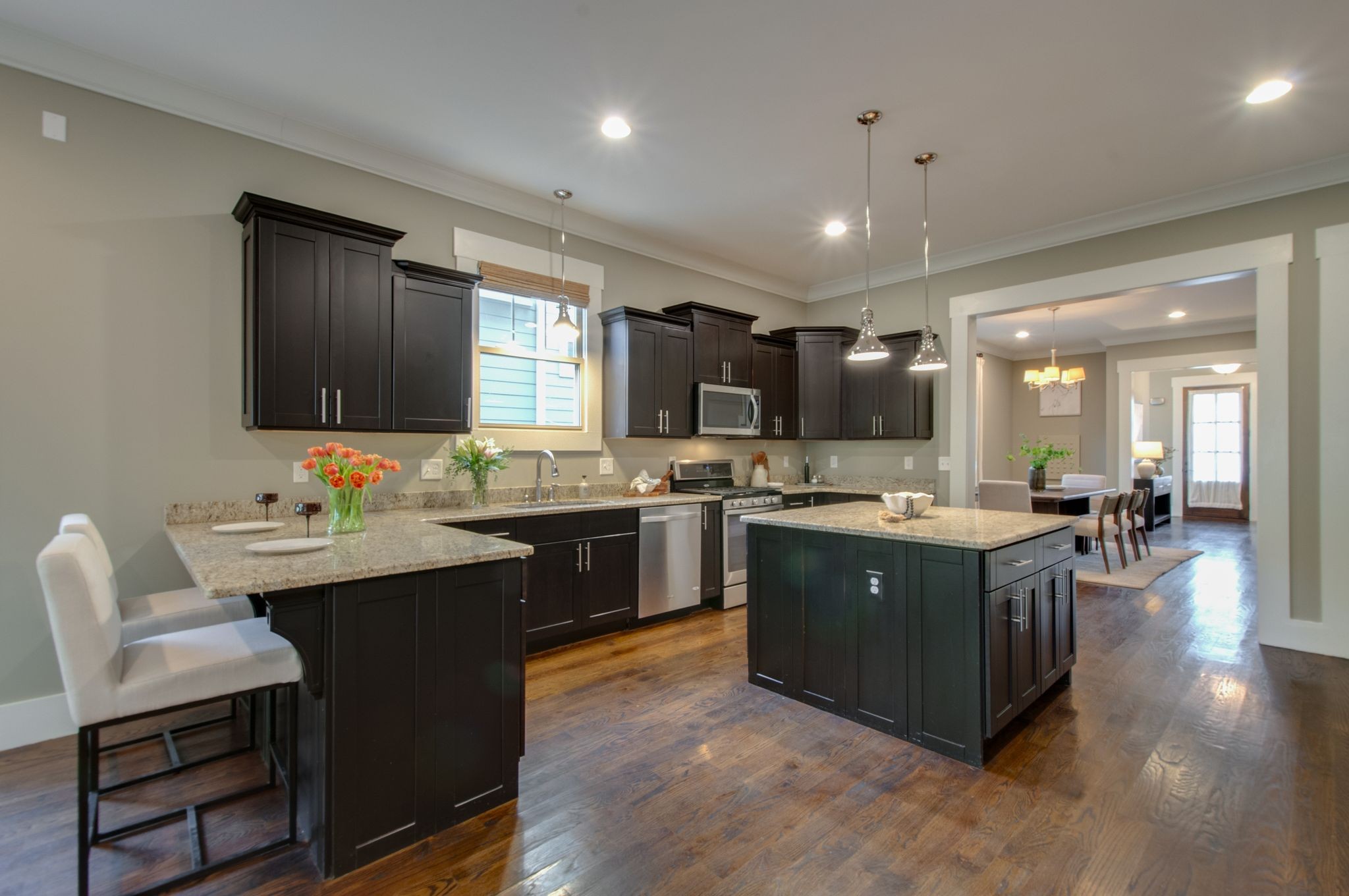 Open-plan kitchen with dark cabinetry, granite island, stainless steel appliances, and hardwood floors.