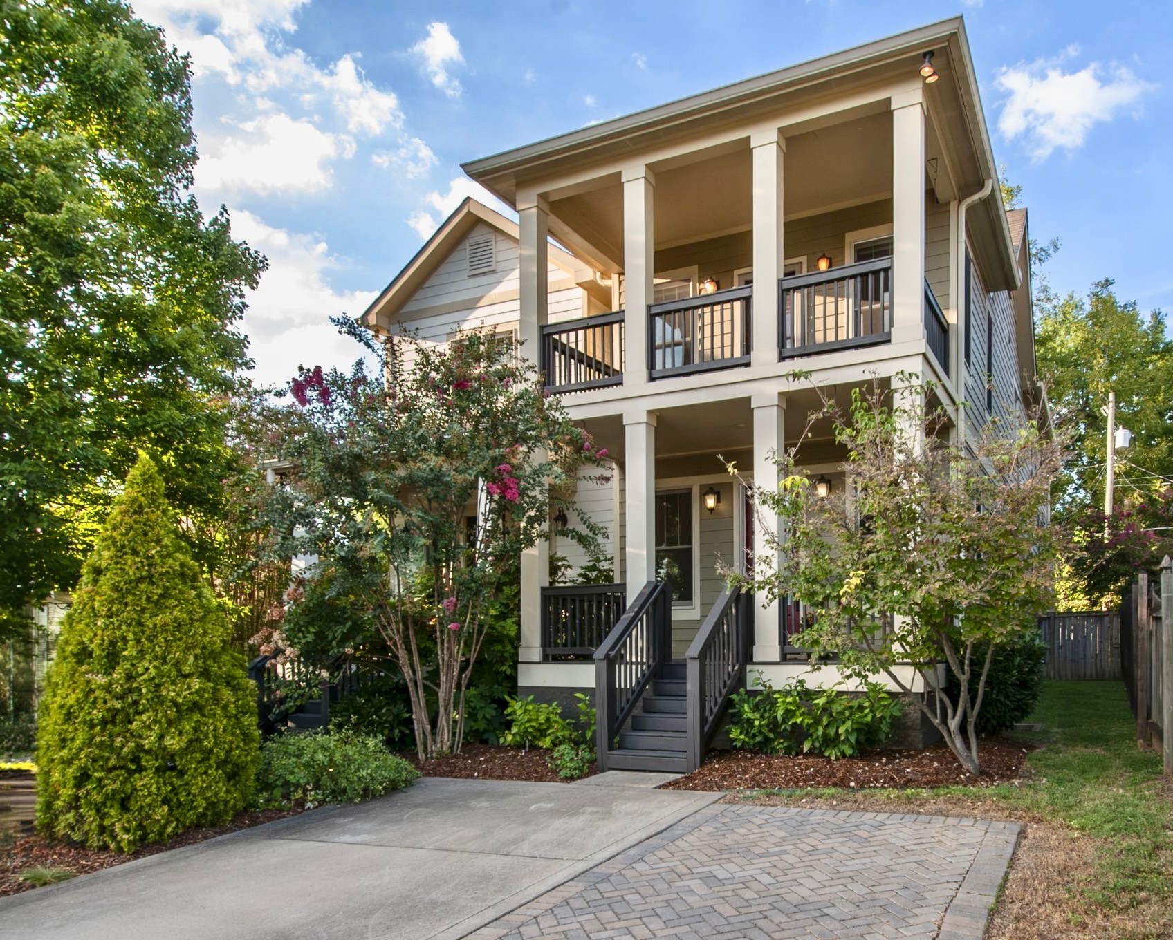 Two-story gray house with broad porches, dark railings, and a landscaped front garden.