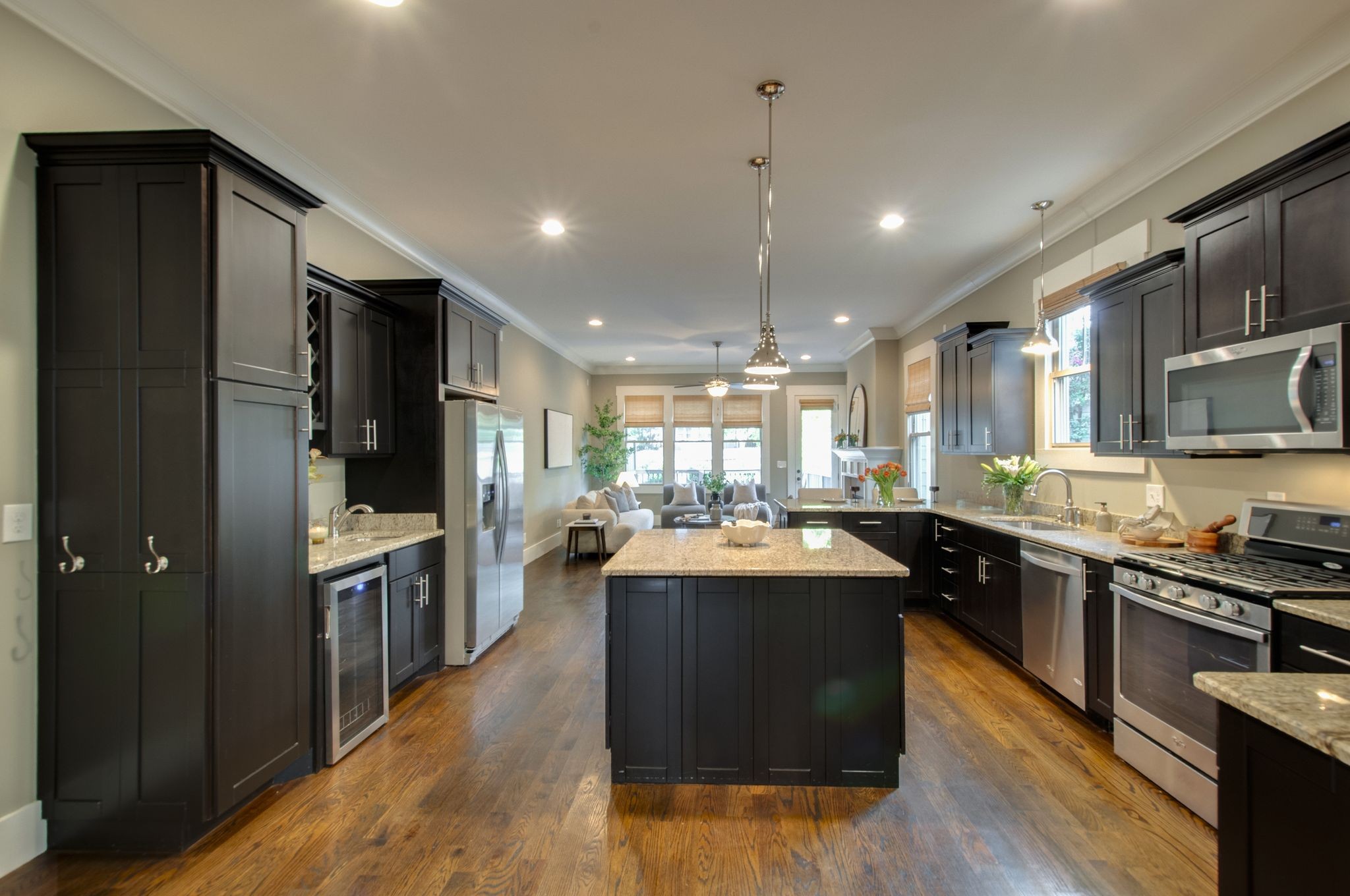 Kitchen with dark cabinets, granite island, stainless appliances, and an opening into a furnished living area.