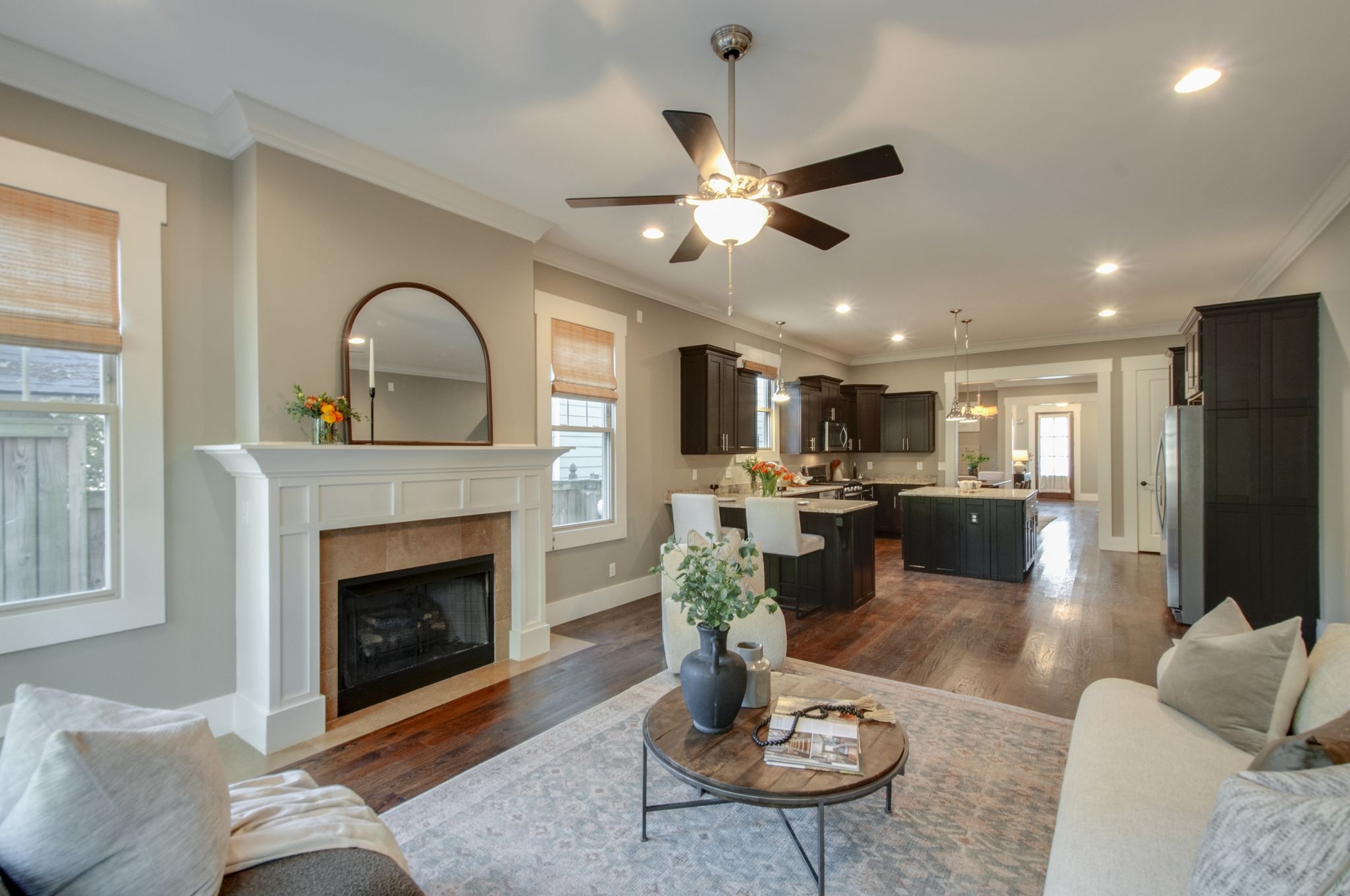 Open-plan living room and kitchen with a fireplace, dark cabinetry, and wood floors.