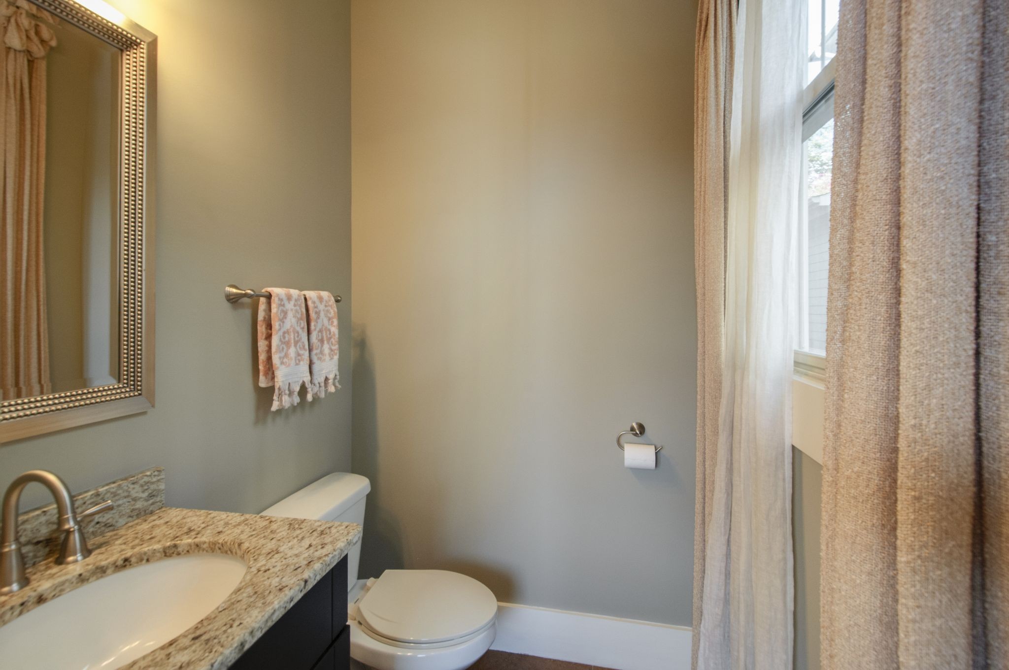 Bathroom with granite vanity, framed mirror, and curtained window.