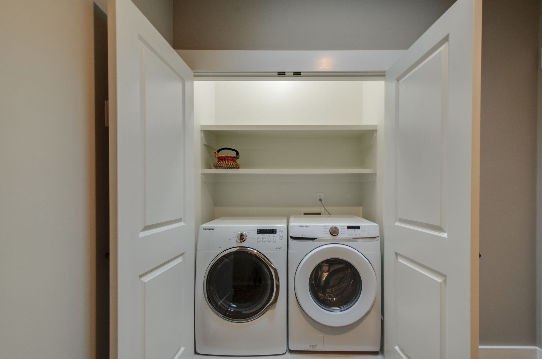 Laundry closet with front-loading washer and dryer beneath built-in shelves.