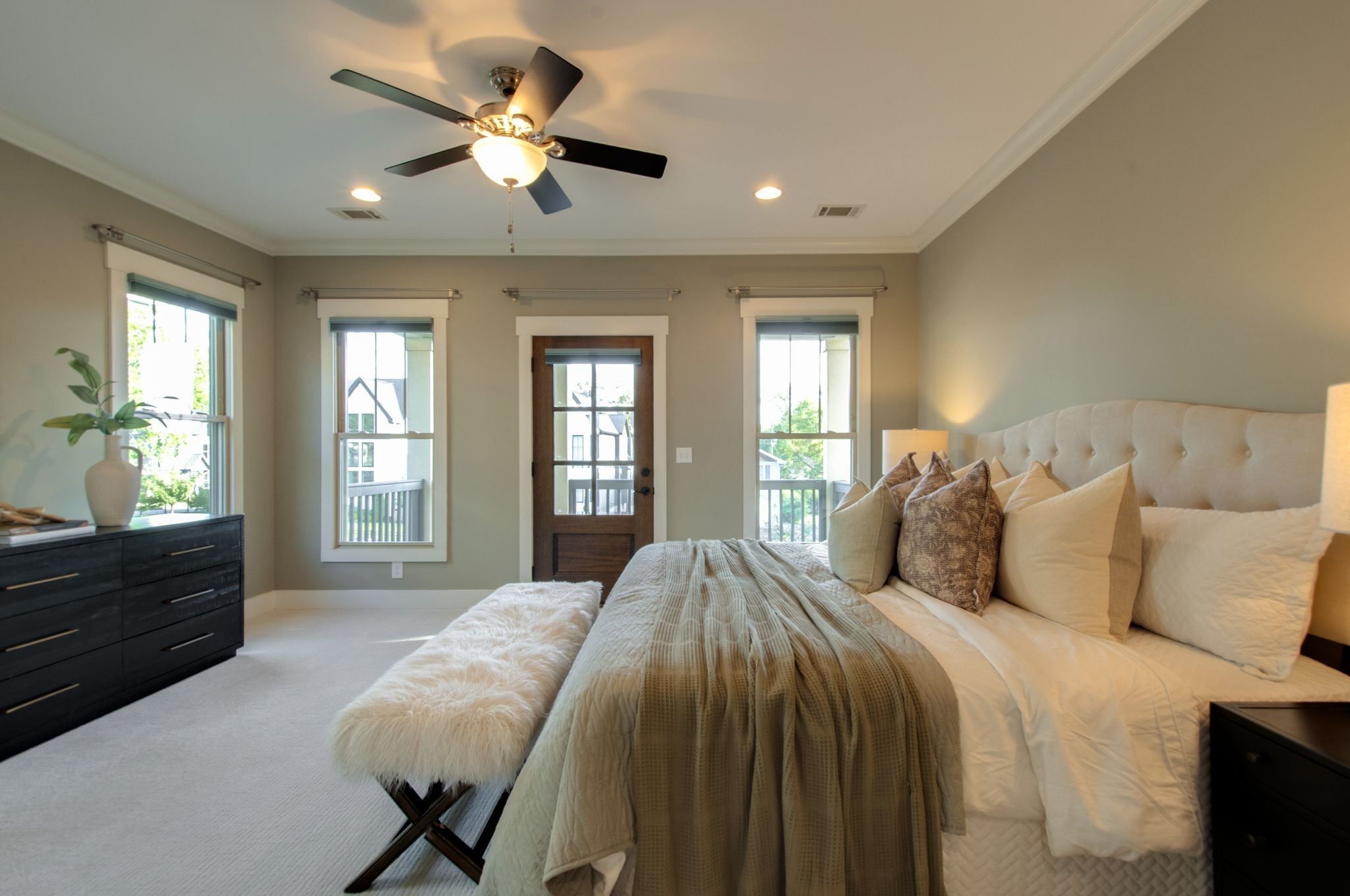 Bedroom with a large upholstered bed, neutral bedding, and windows flanking a glass-paneled door.