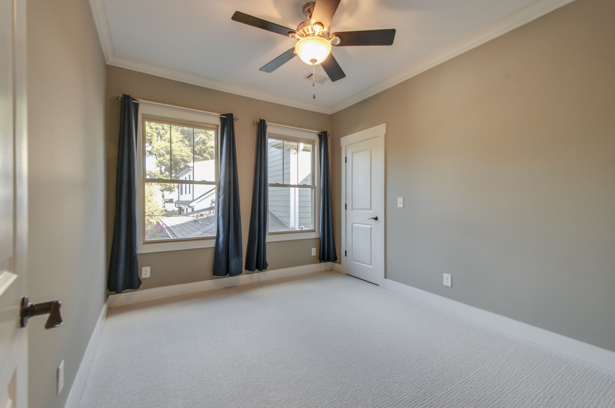 Vacant bedroom with two curtained windows, light carpet, and a ceiling fan.
