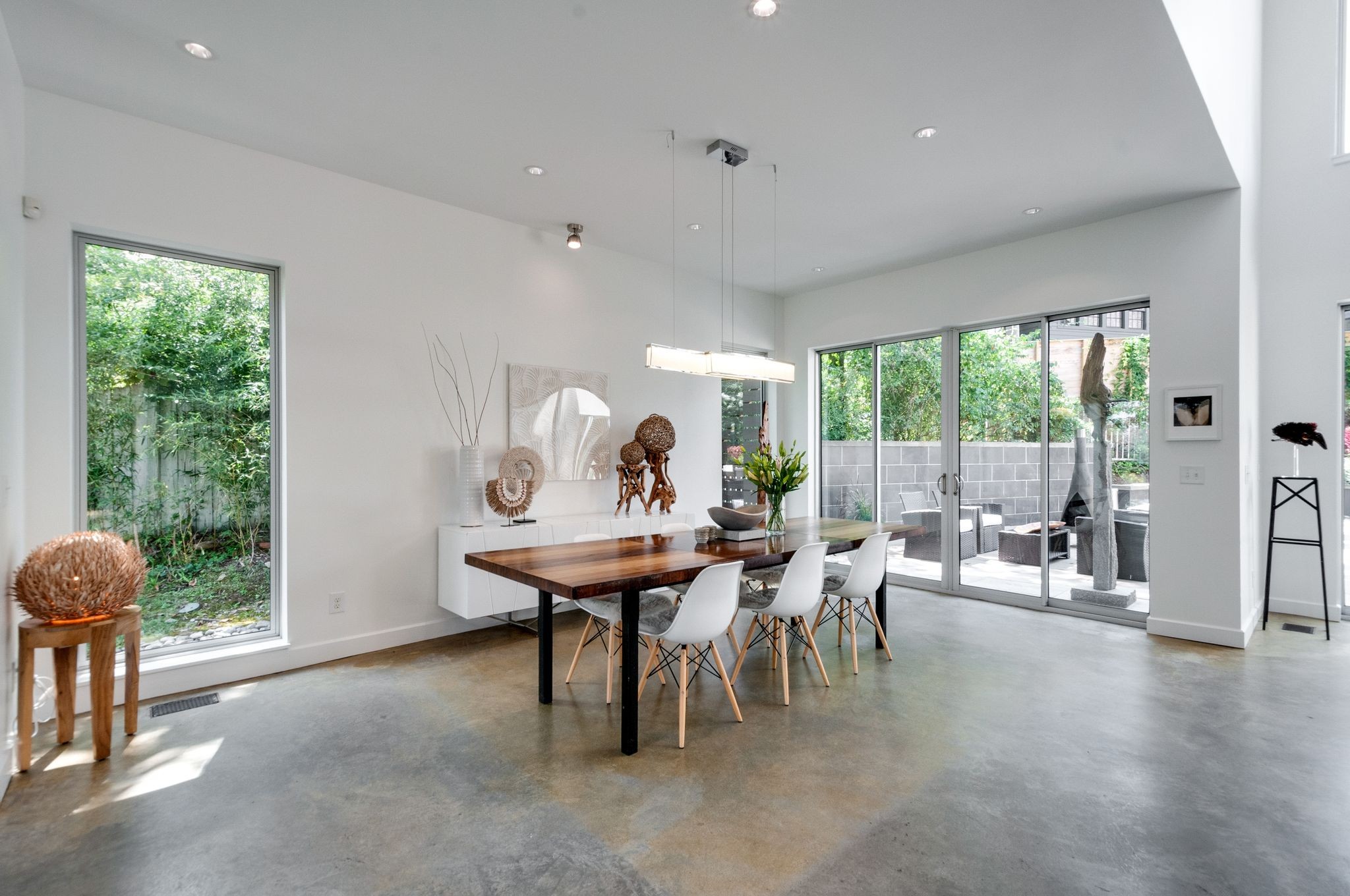 Dining room with a long wood table, white chairs, and sliding glass doors to a patio.