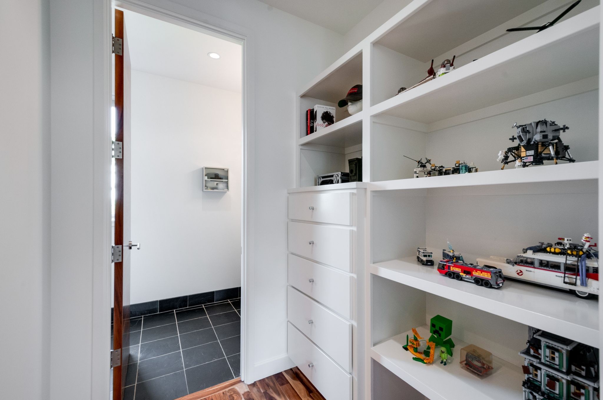 Built-in white shelving and drawers display model vehicles and toys beside an open doorway.