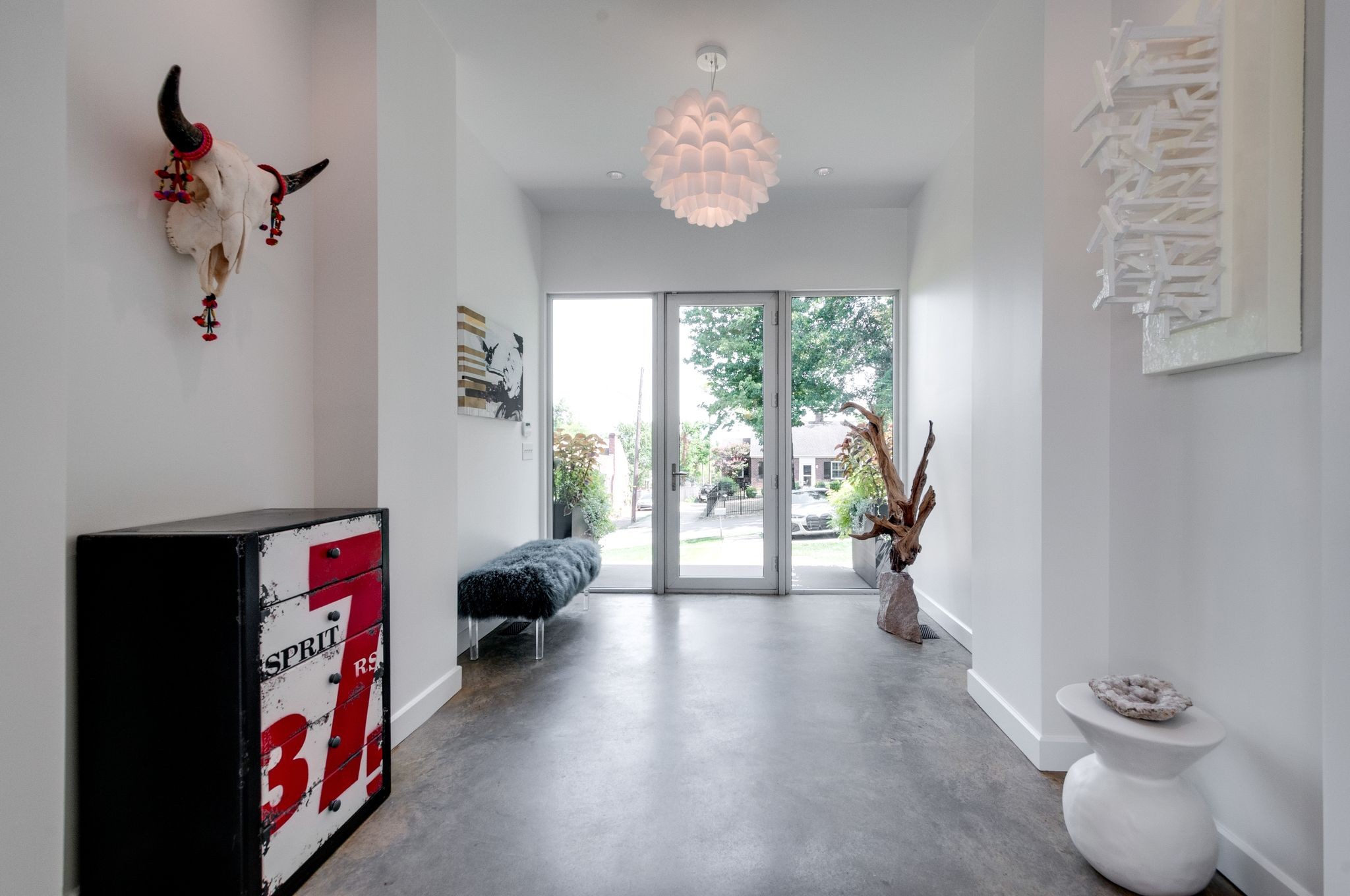Modern entryway with concrete floors, glass doors, sculptural pendant, and eclectic wall art.