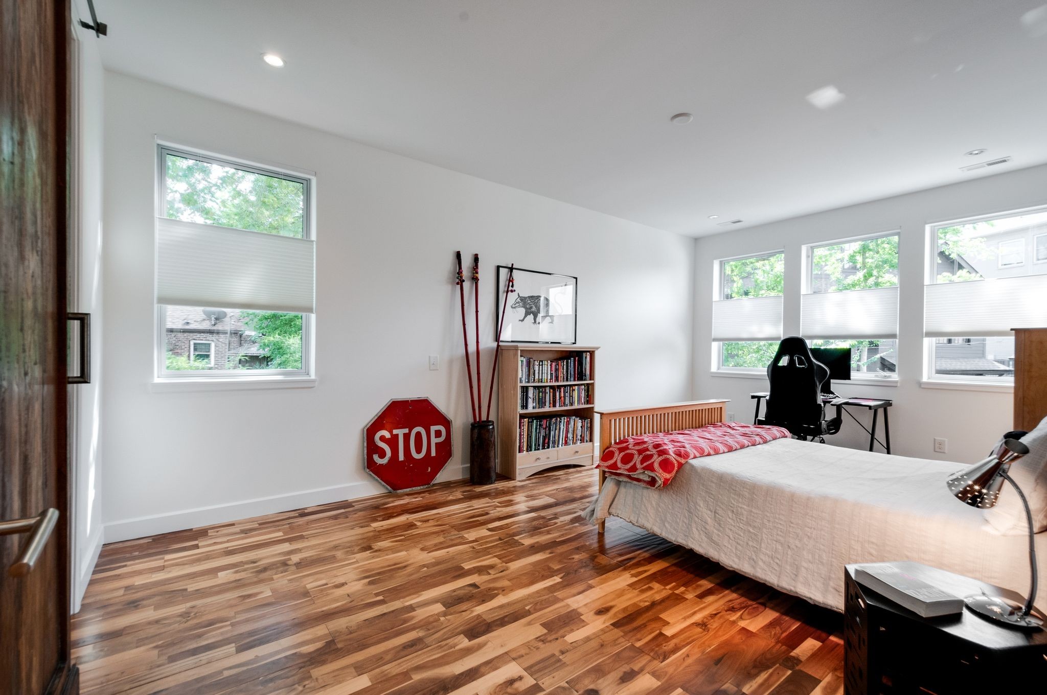 Bedroom with wide-plank wood floors, a white bed, multiple windows, and a red STOP sign.