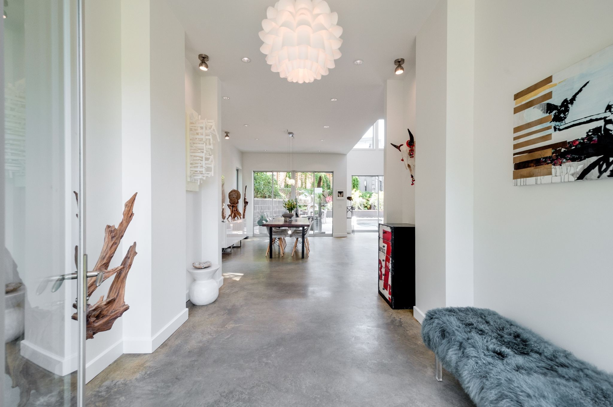 Open-plan entry hall with polished concrete floors, sculptural pendant, and dining area beside garden-facing glass doors.