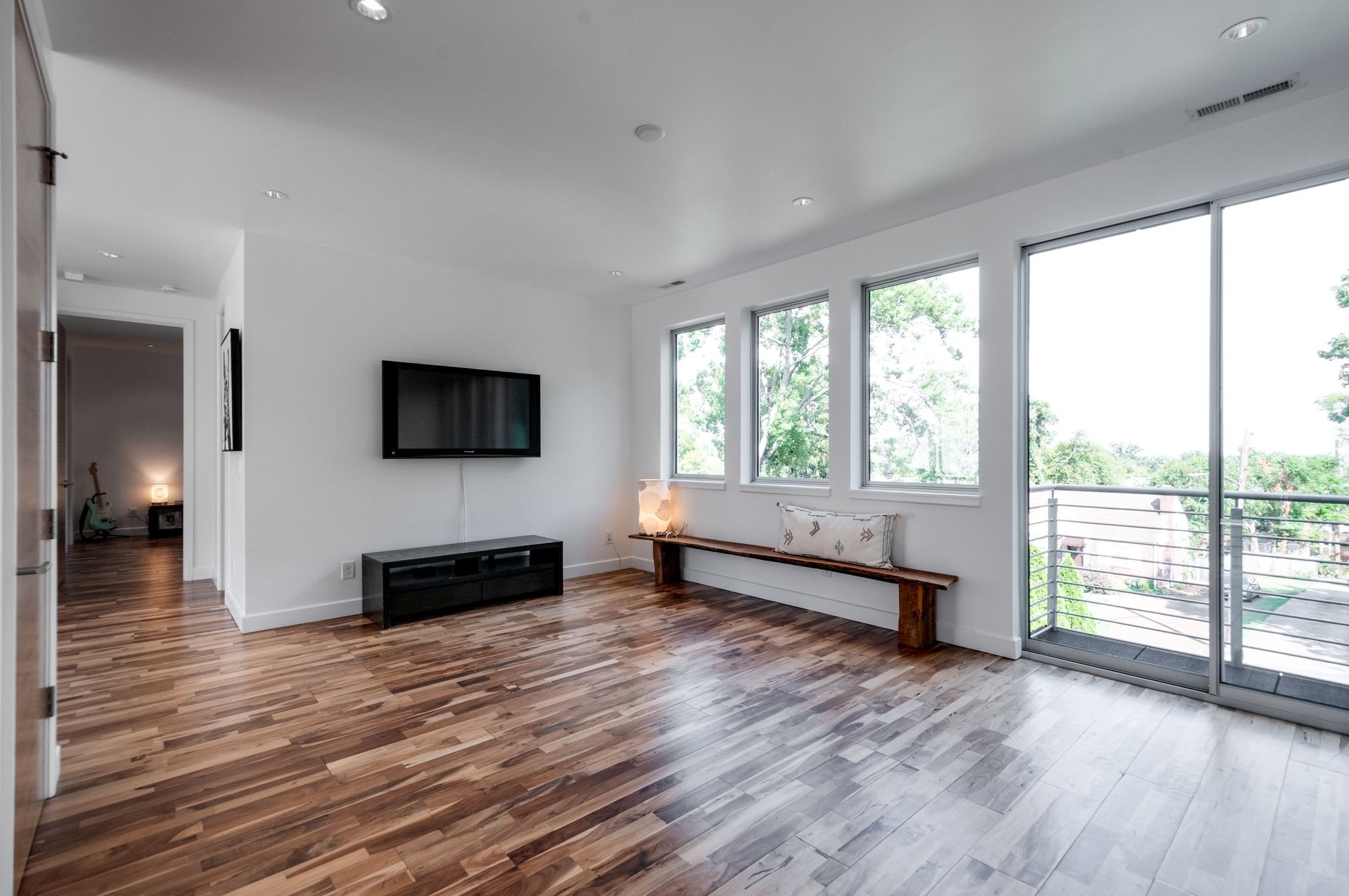 Living room with wood floors, a wooden bench, and large windows beside a balcony.