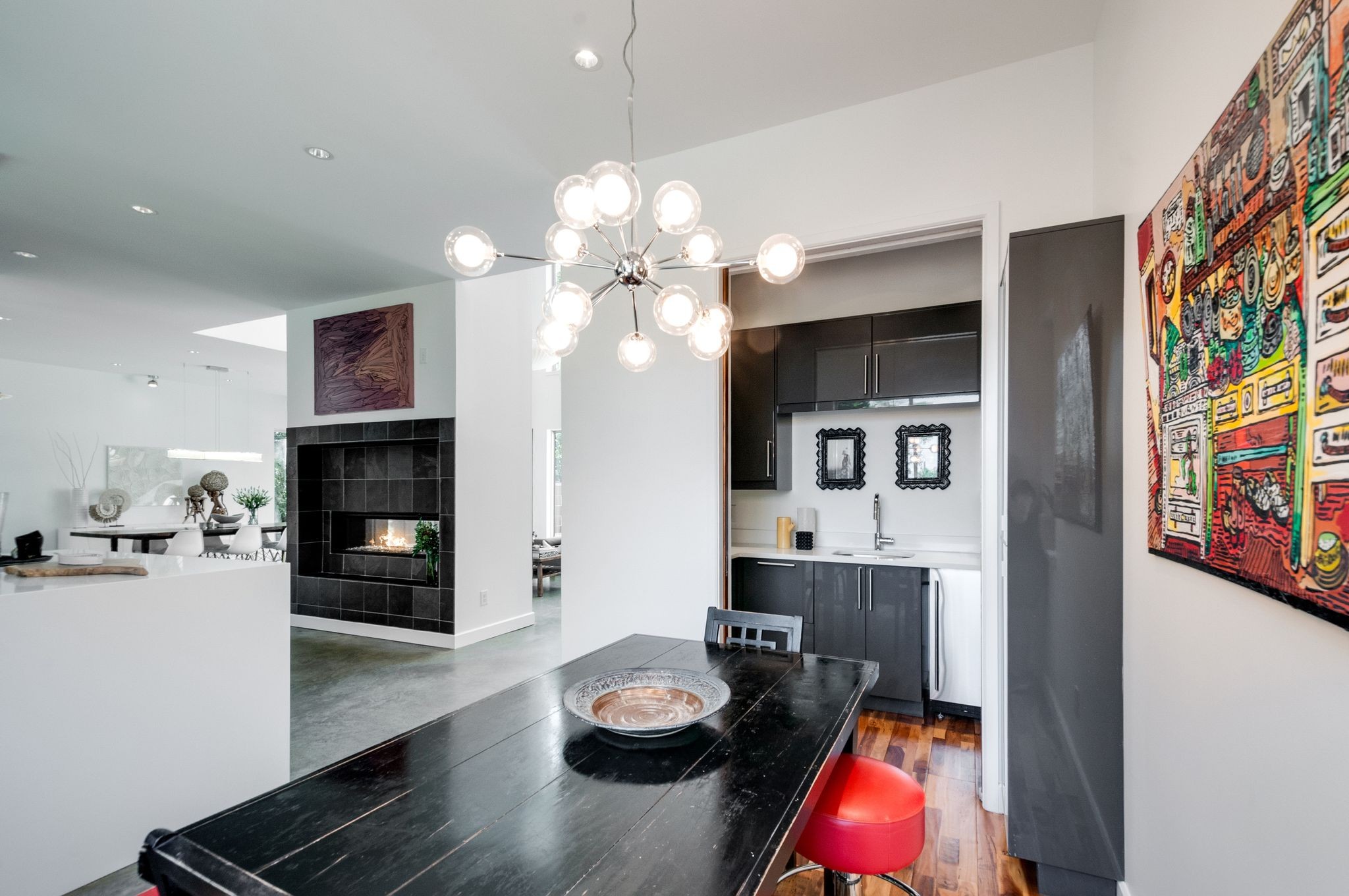 Open-plan dining area with a black table, red stools, dark kitchen cabinets, and tiled fireplace.