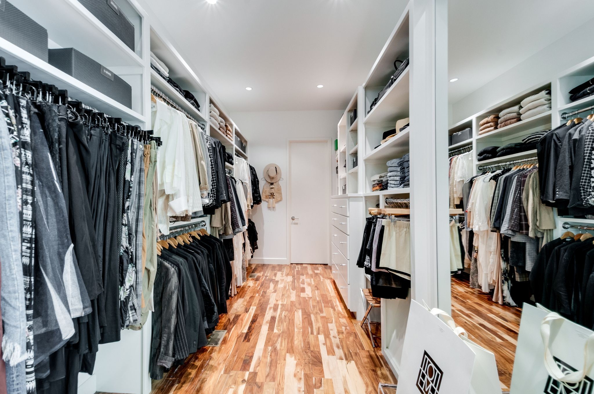 Walk-in closet with built-in shelving, neatly arranged clothes, a full-length mirror, and wood flooring.