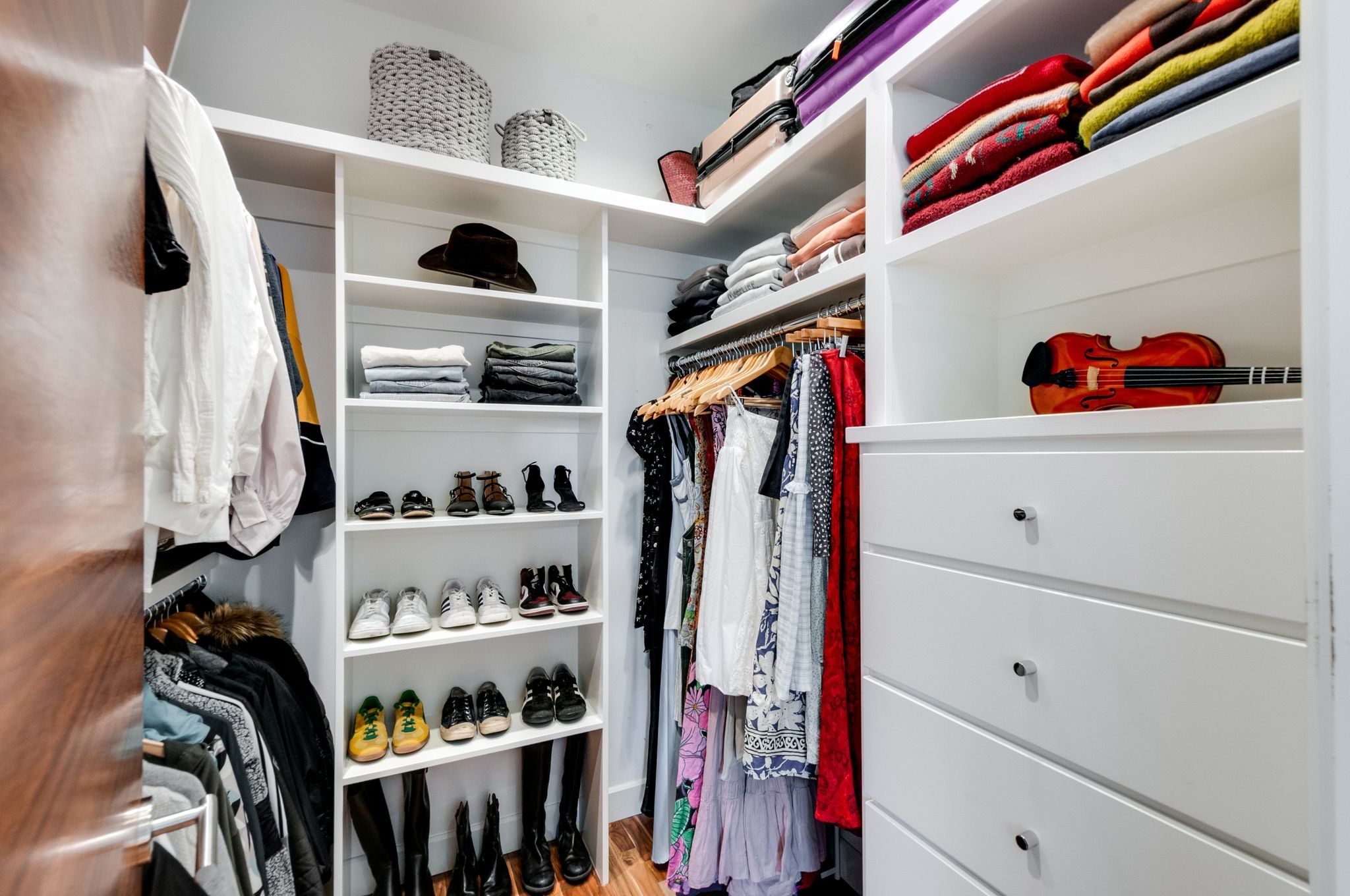 Walk-in closet with white built-in shelving, organized clothing and shoes, and a violin on display.