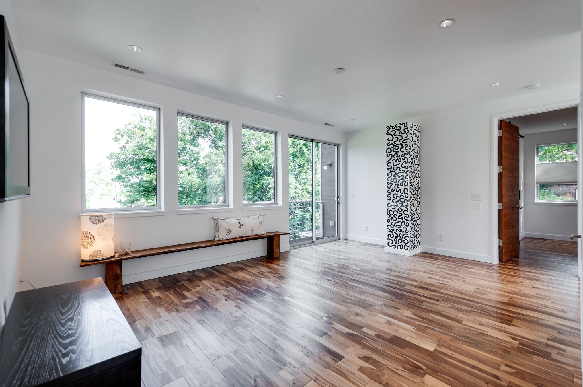 Bright living room with wide-plank floors, a window-side bench, and a glass door to the balcony.