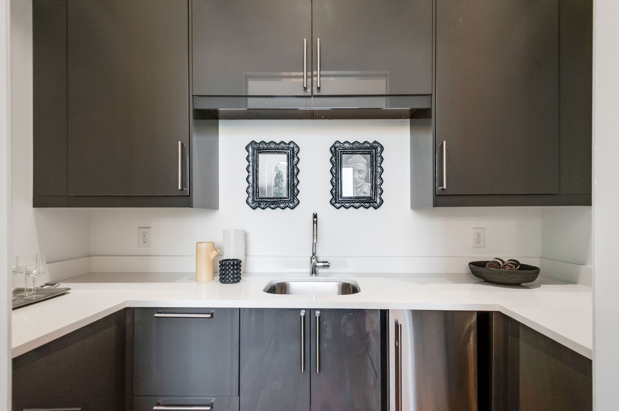 Compact kitchen with dark cabinets, white counters, and a small sink beneath framed artwork.