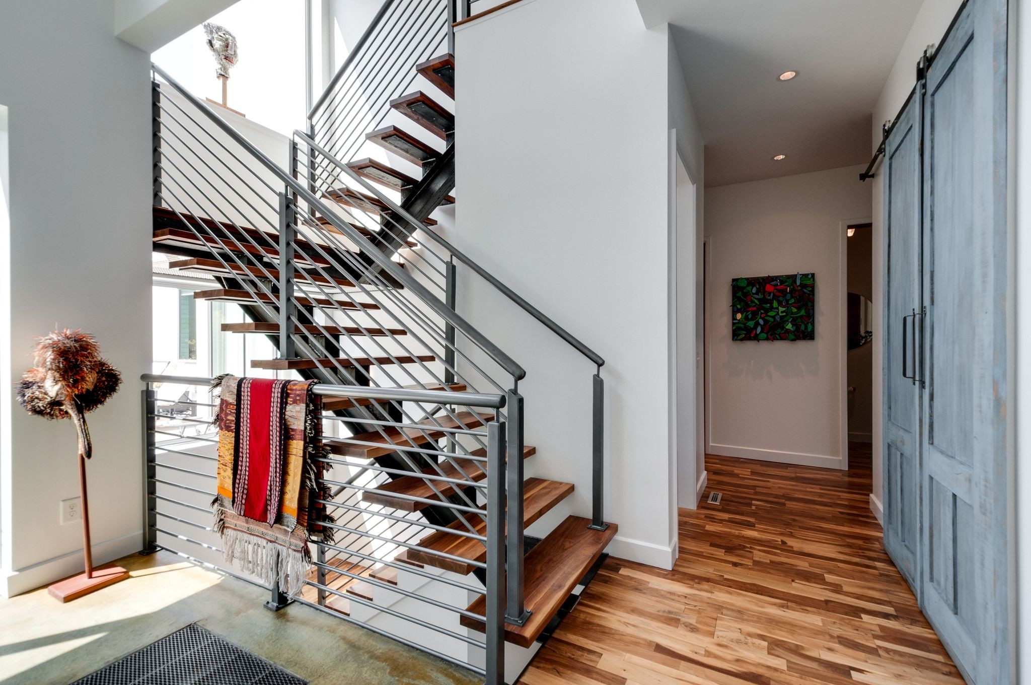 Entryway with open-riser wood staircase, metal railings, hardwood floors, and a blue sliding barn door.