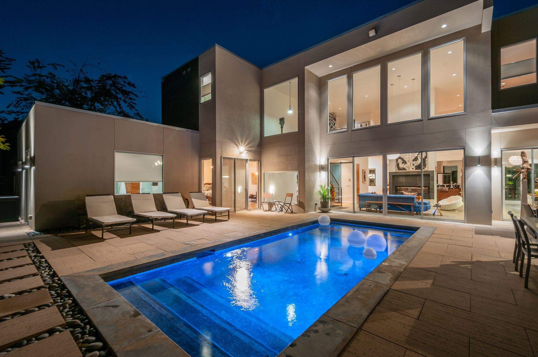 Modern home exterior at night with an illuminated swimming pool and patio loungers.