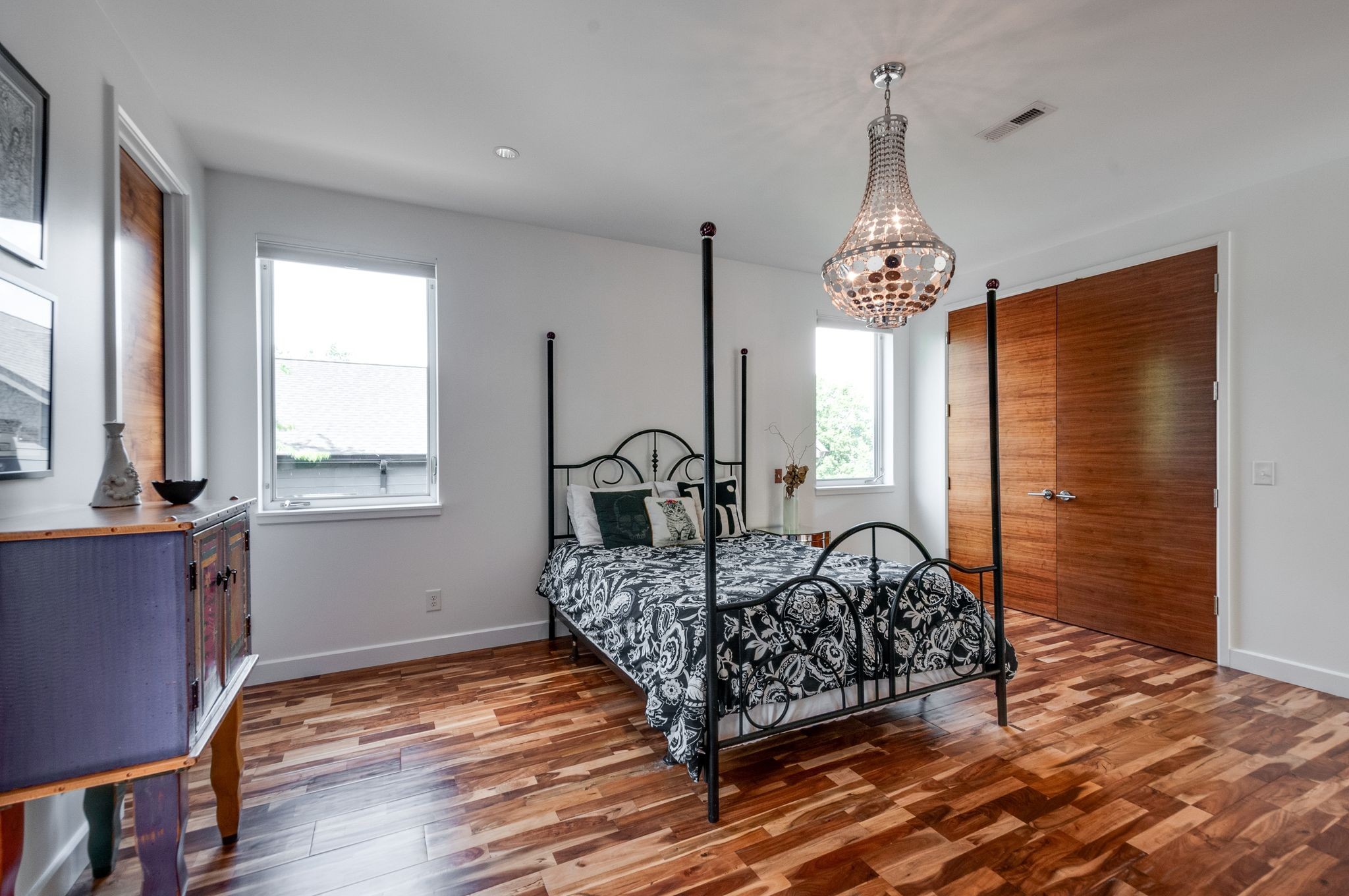 Bedroom with a black iron four-poster bed, patterned bedding, wood floors, and a crystal chandelier.