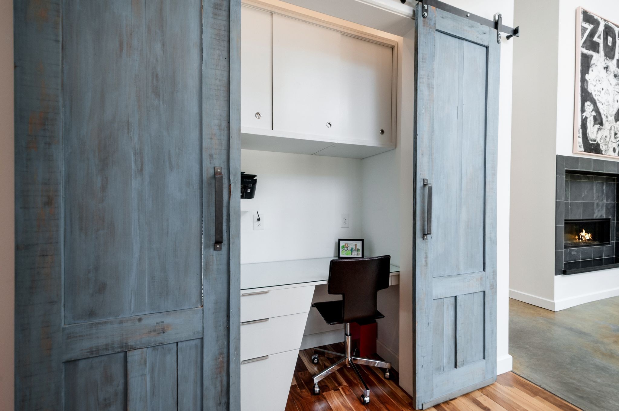 Home office nook with blue sliding barn doors, a built-in desk, and a dark rolling chair.