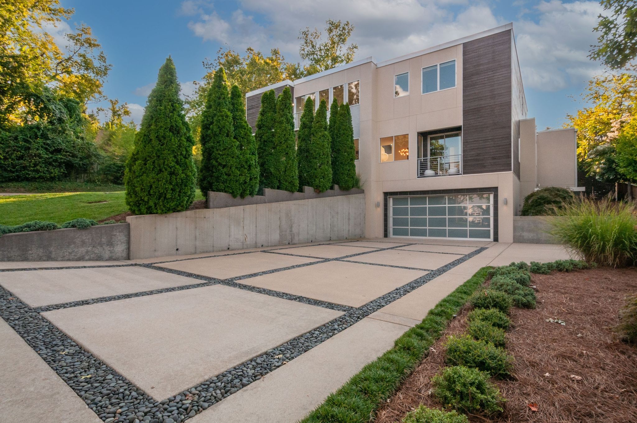 Modern two-story home with a glass-panel garage door and a stone-grid concrete driveway.